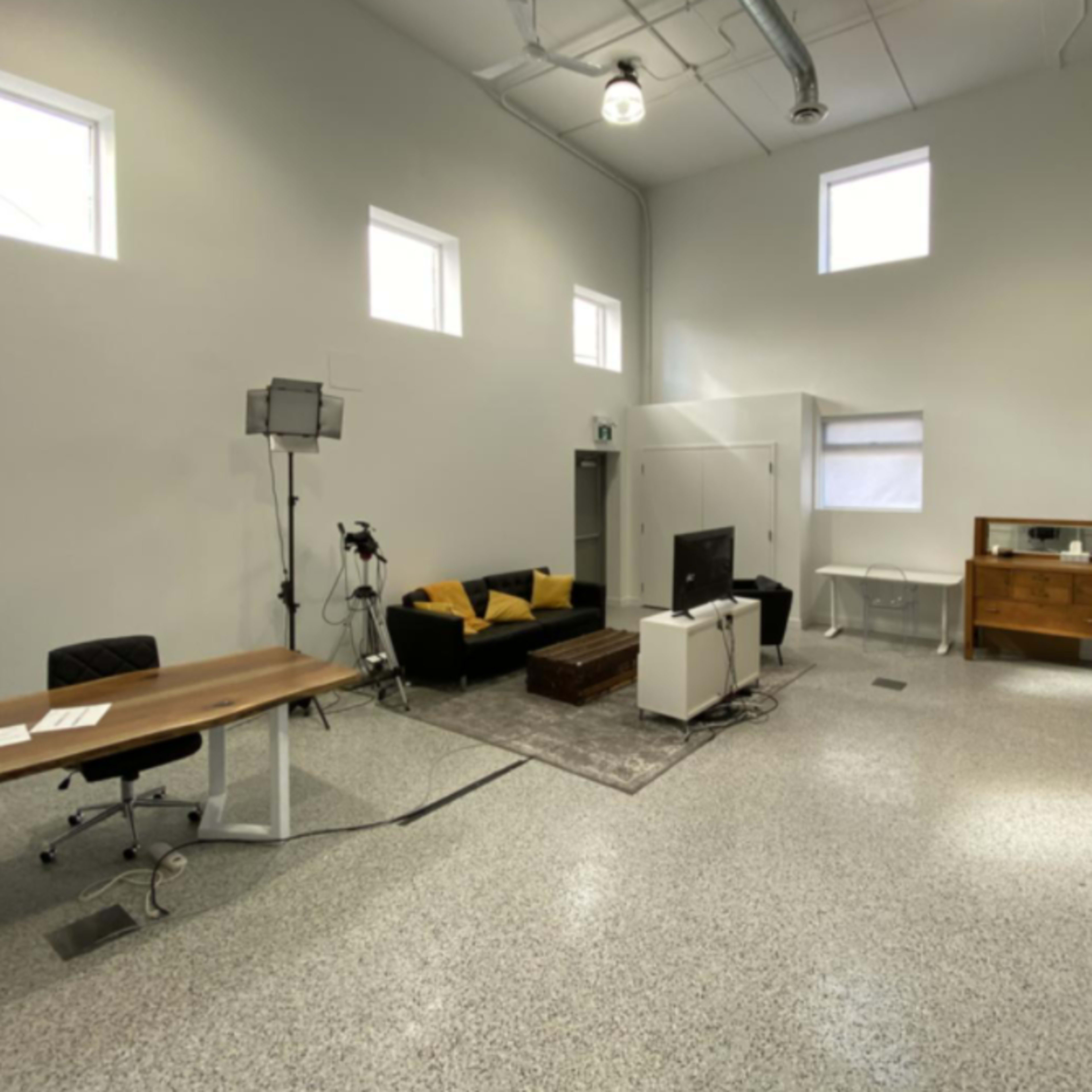 A spacious, minimalistic room featuring a couch, a television, a table with chairs, and a wooden cabinet.
