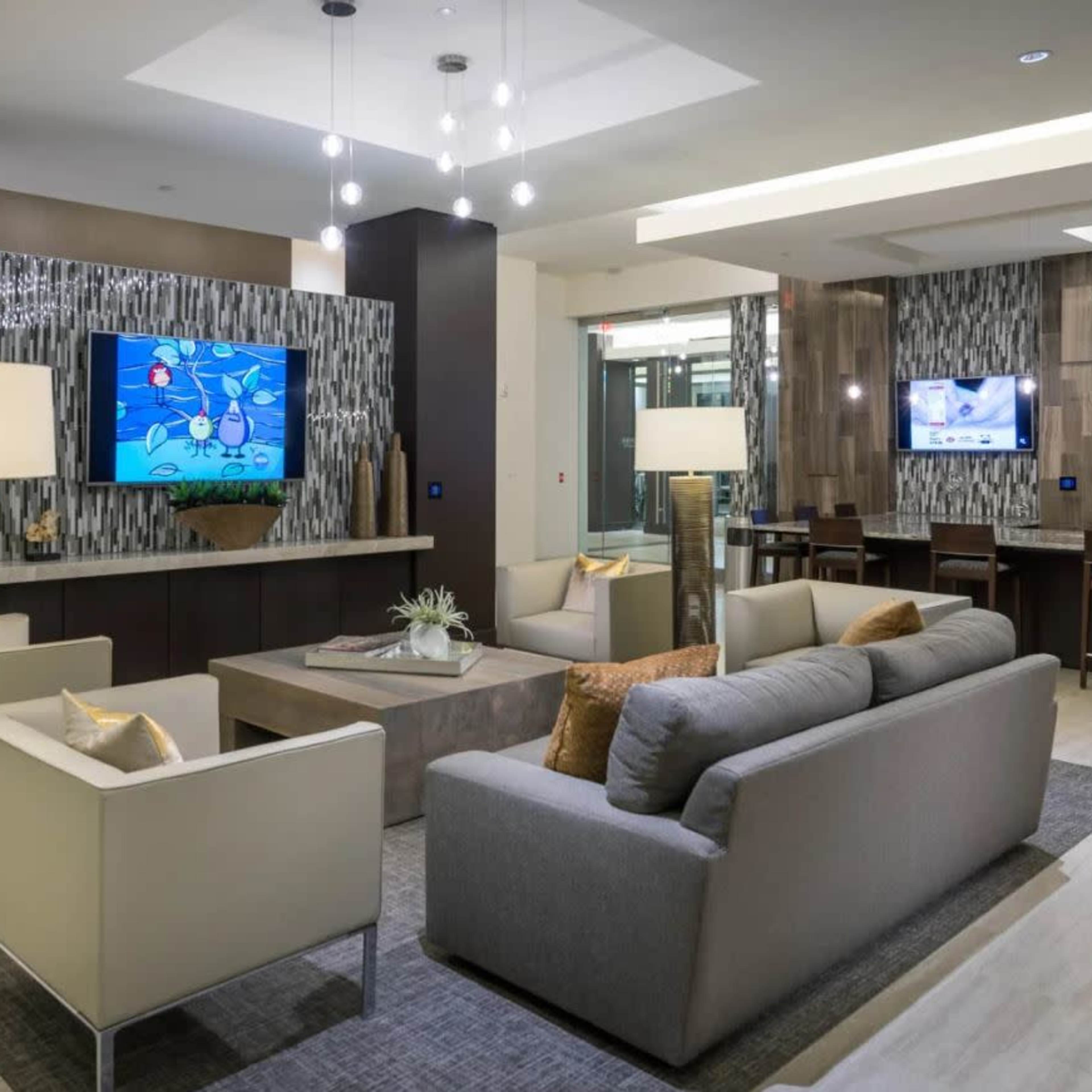 A modern lobby with couches, decorative lighting, and a large television displaying graphics on the wall.