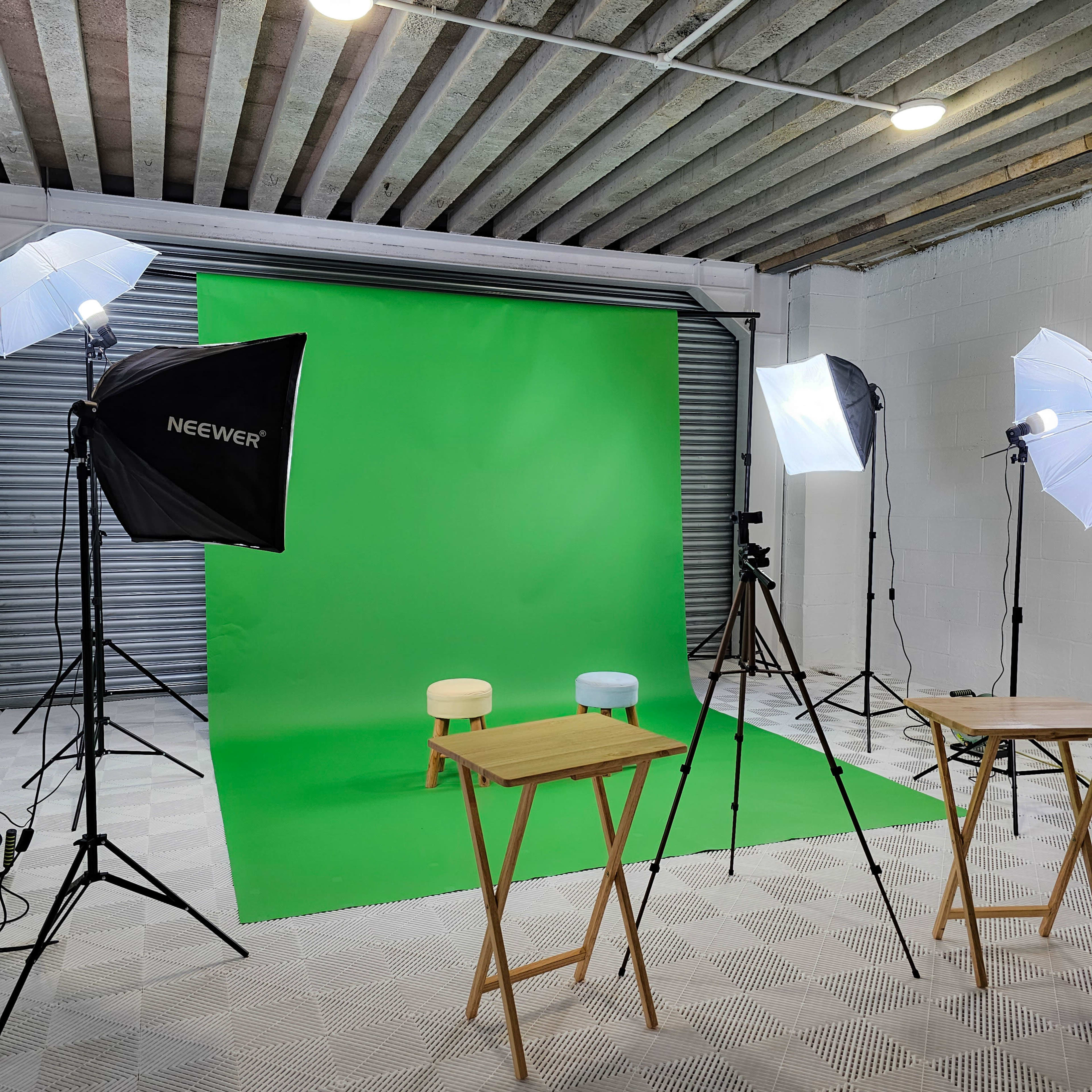 A photography studio setup featuring a green backdrop, two small stools, and lighting equipment on tripods.