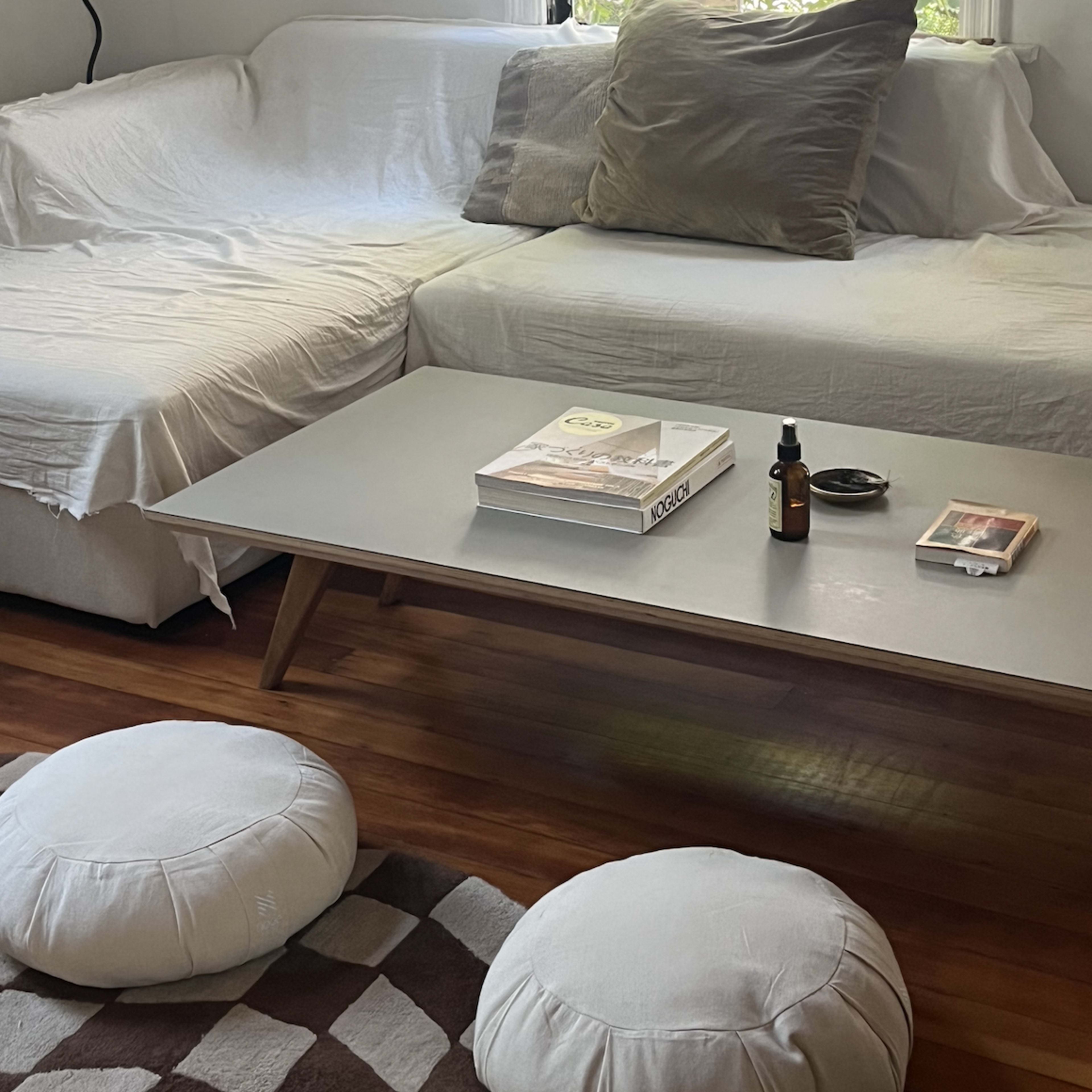 A living room with a sectional couch covered in white fabric, a coffee table, and two round cushions on a patterned rug.
