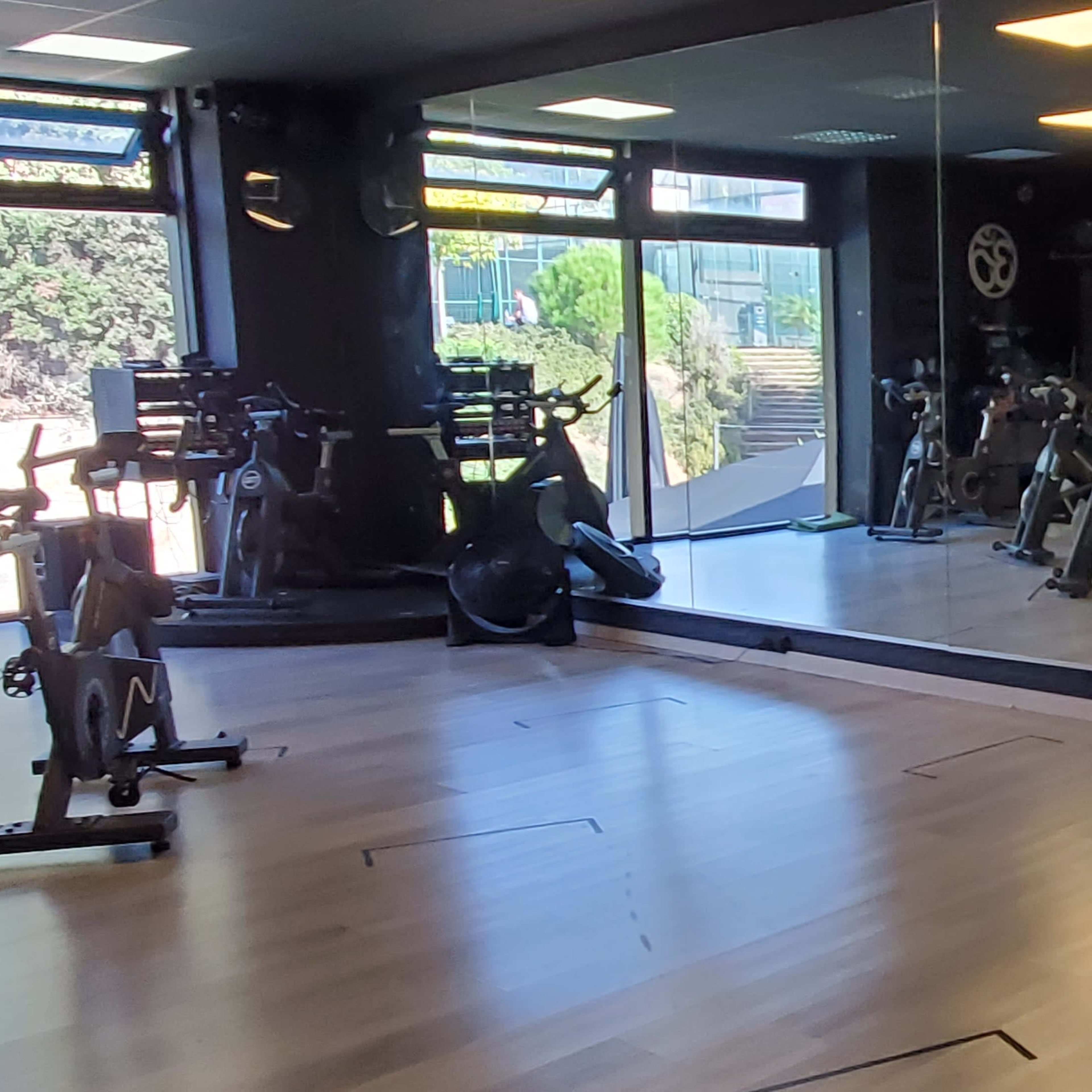A fitness studio with exercise bikes lined against a wall, large mirrors reflecting the space, and green exercise balls on a shelf.