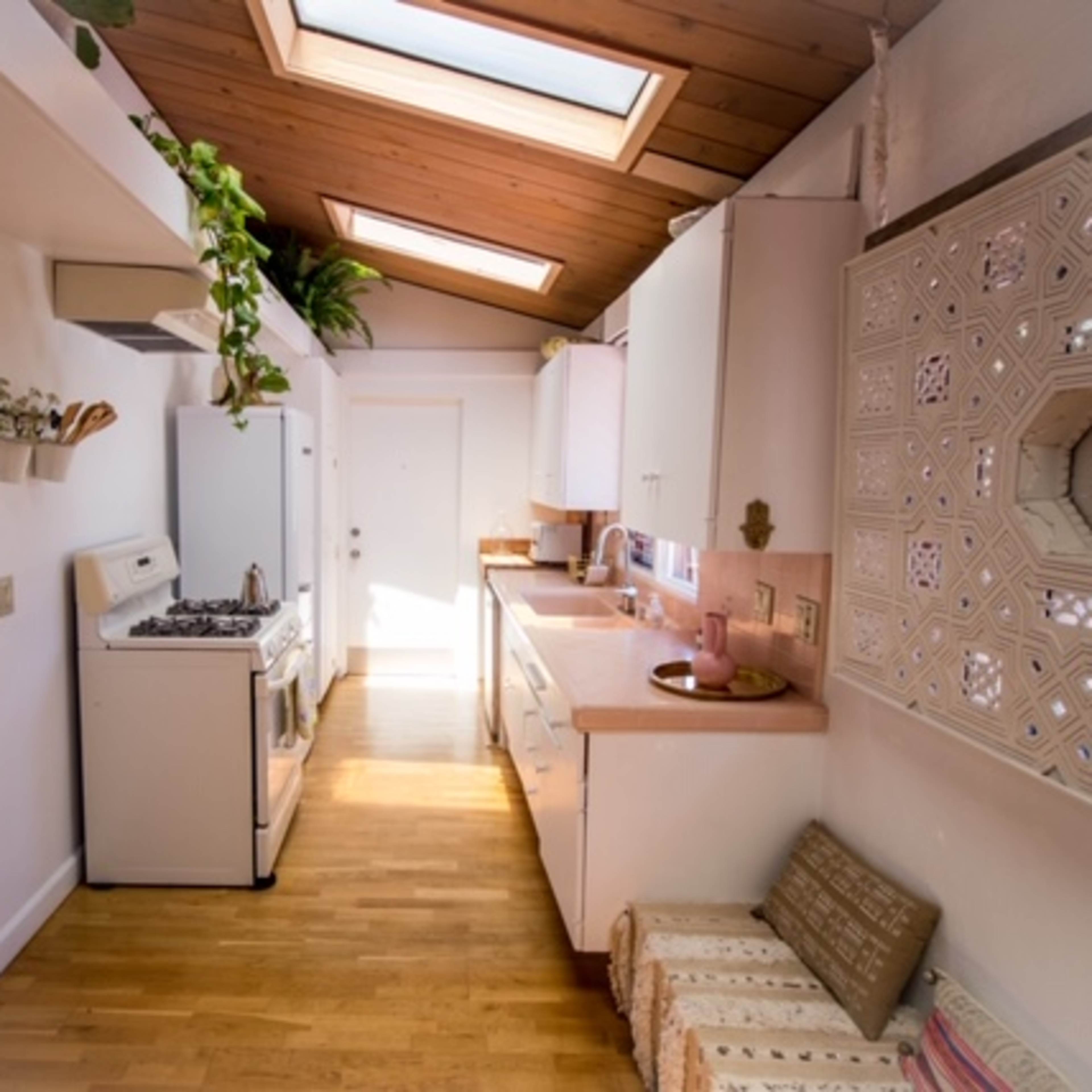 A narrow kitchen with skylights, white cabinets, a gas stove, and wooden flooring.