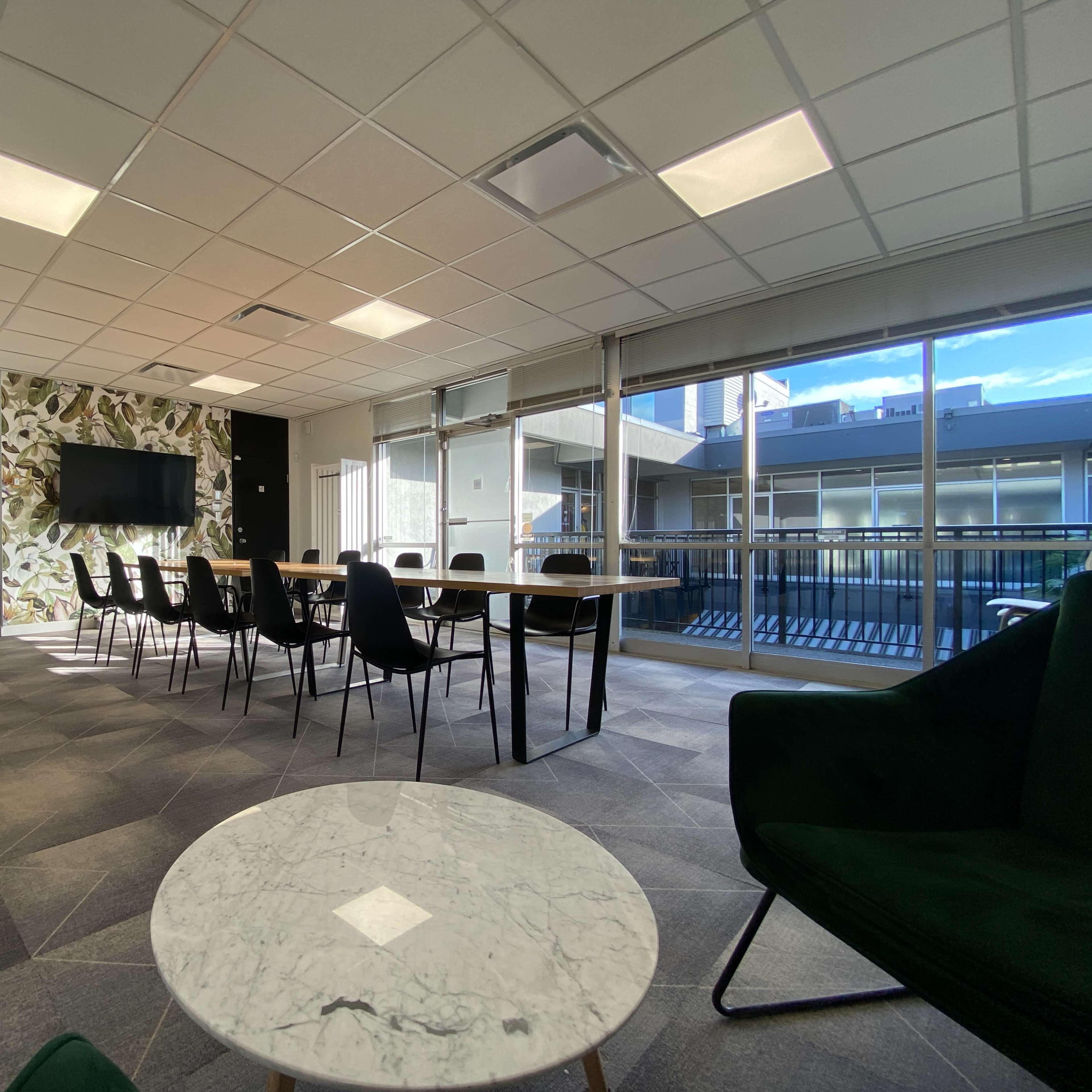 A modern conference room features a long wooden table surrounded by black chairs, with a whiteboard and a large screen on one wall.