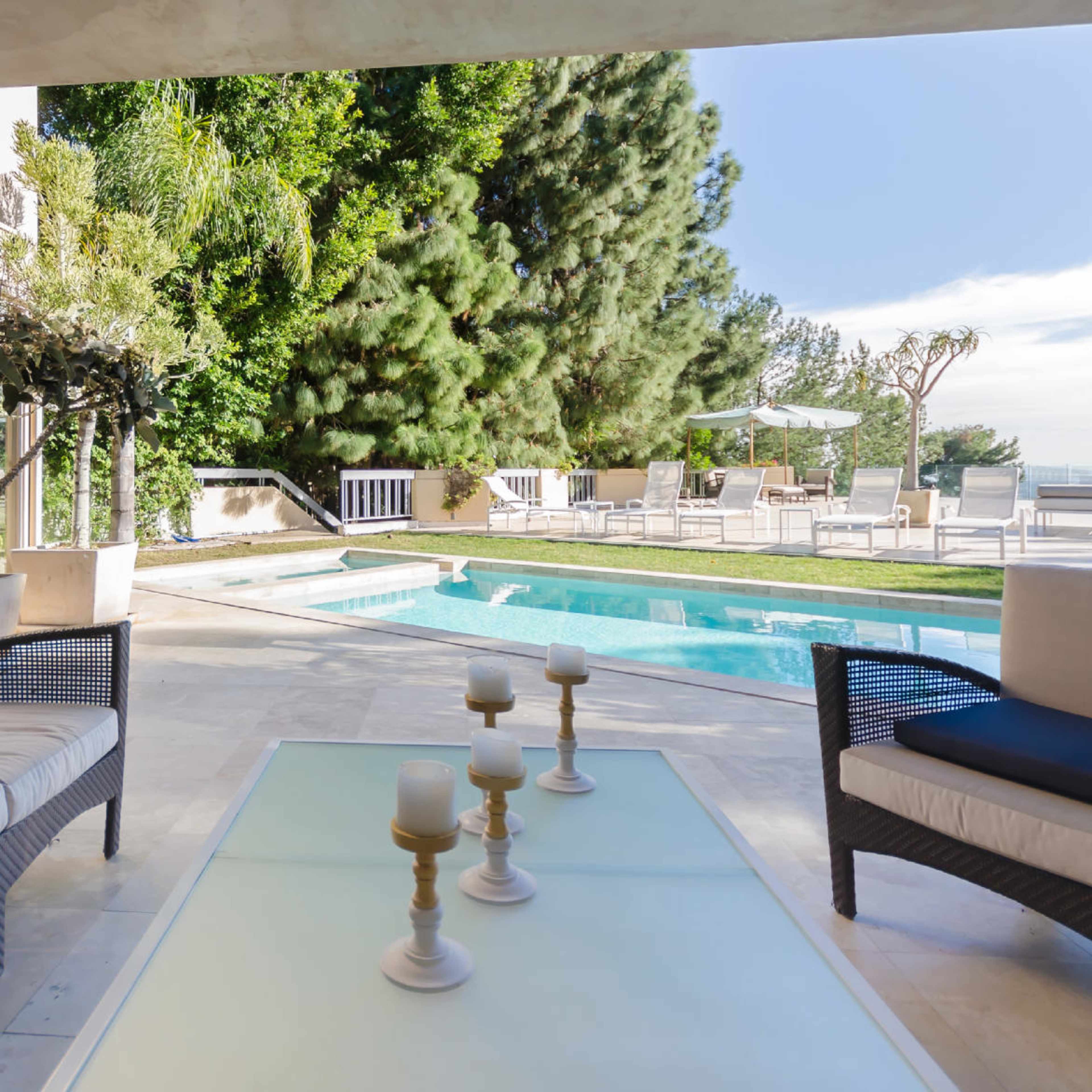 A patio with two seating areas overlooking a swimming pool surrounded by greenery.