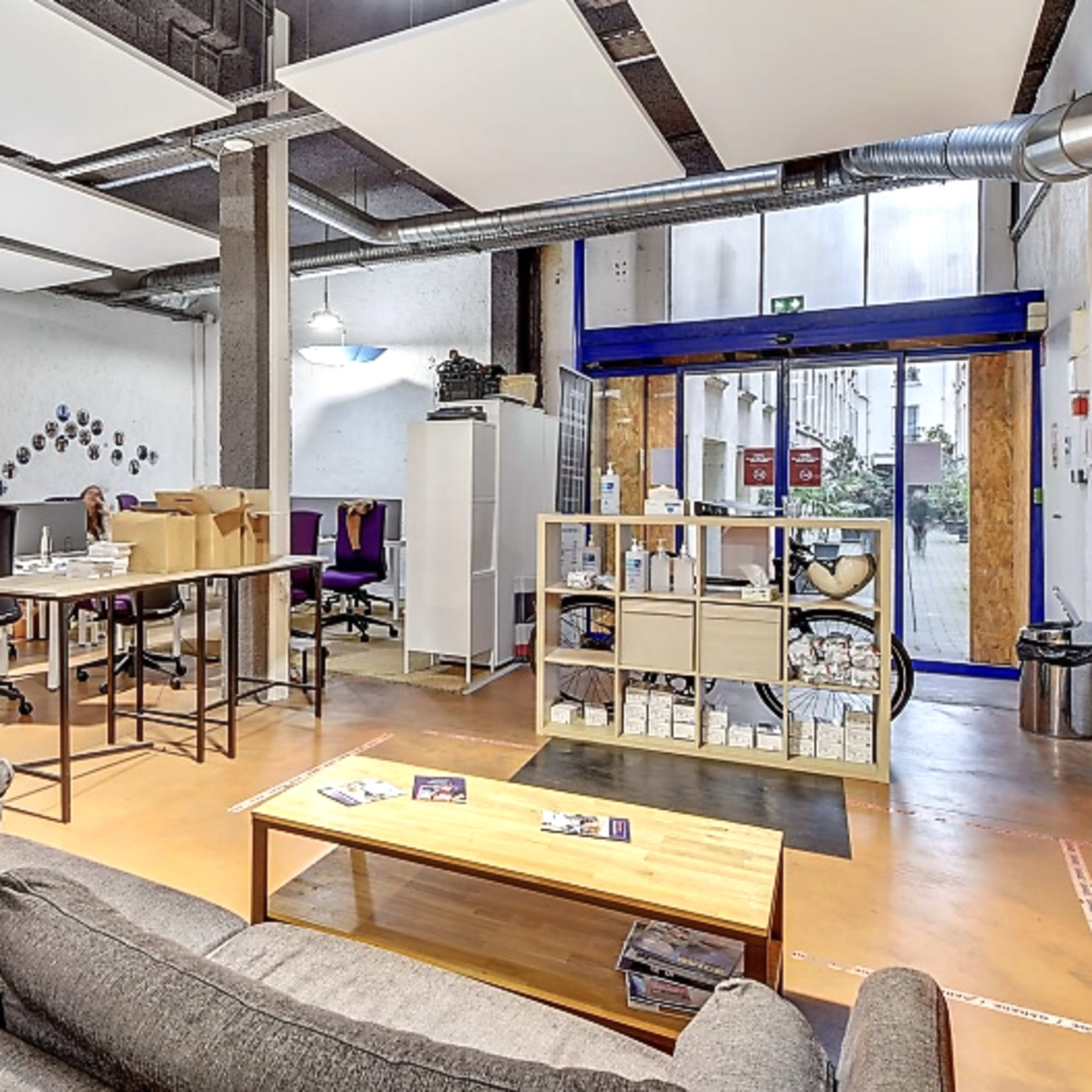 A modern office space with a seating area, workstations, and organized shelving units.