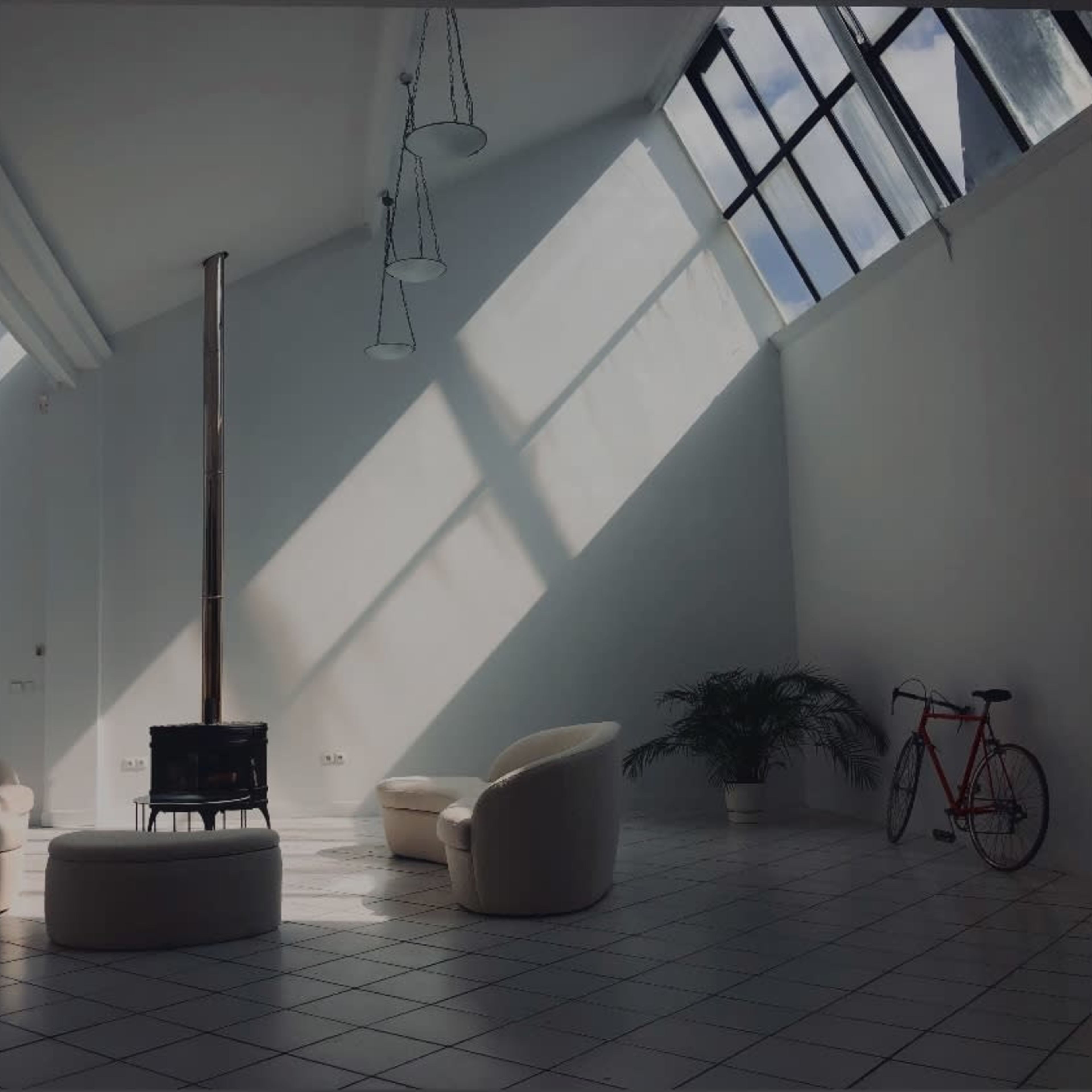 A bright, modern room with two circular chairs, a round table, a wood-burning stove, a potted plant, and a bicycle against a white wall.