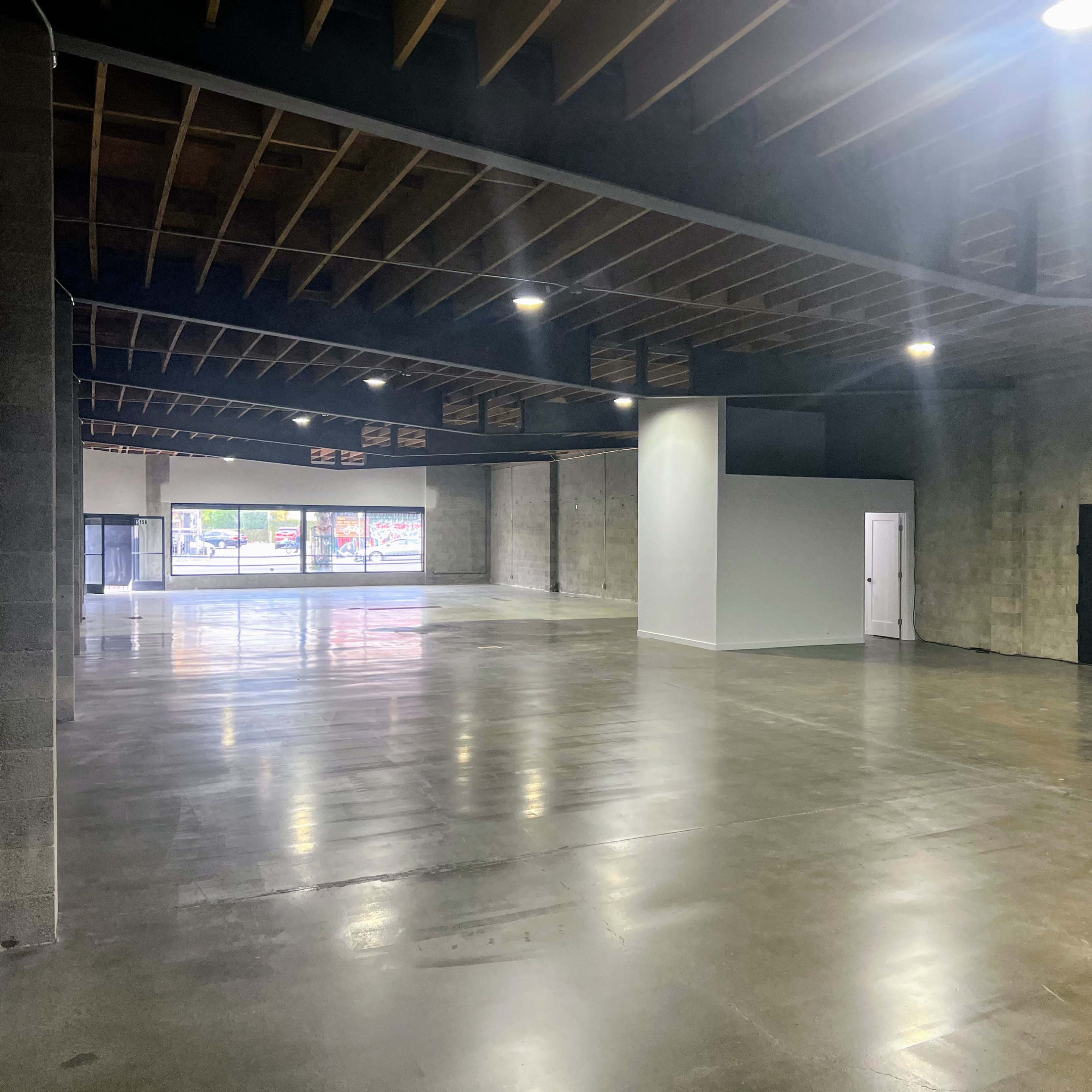 A spacious, empty commercial interior with polished concrete floors and minimal lighting.