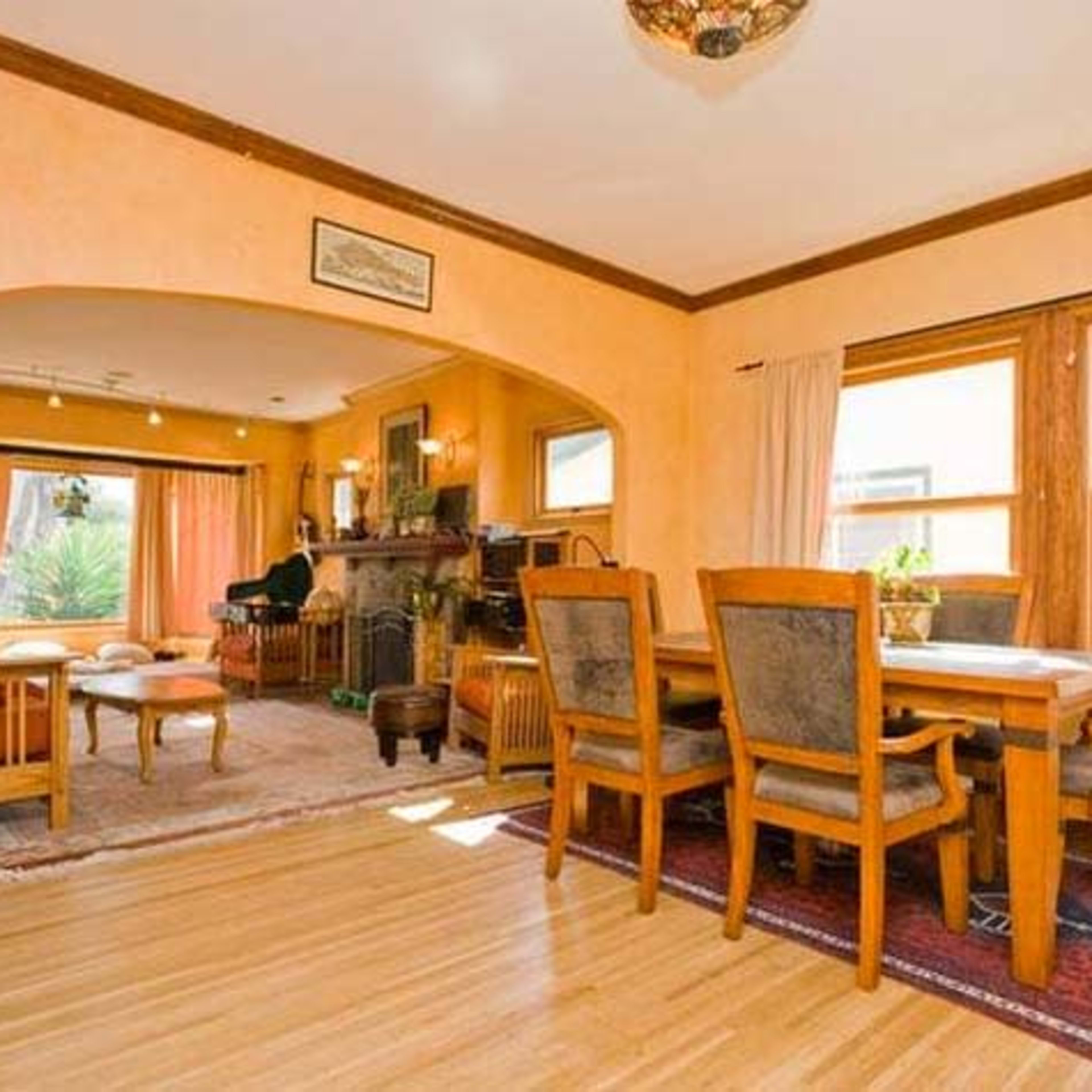 A well-lit dining area with wooden furniture, an arched entryway, and a view of a living room featuring a fireplace and large windows.