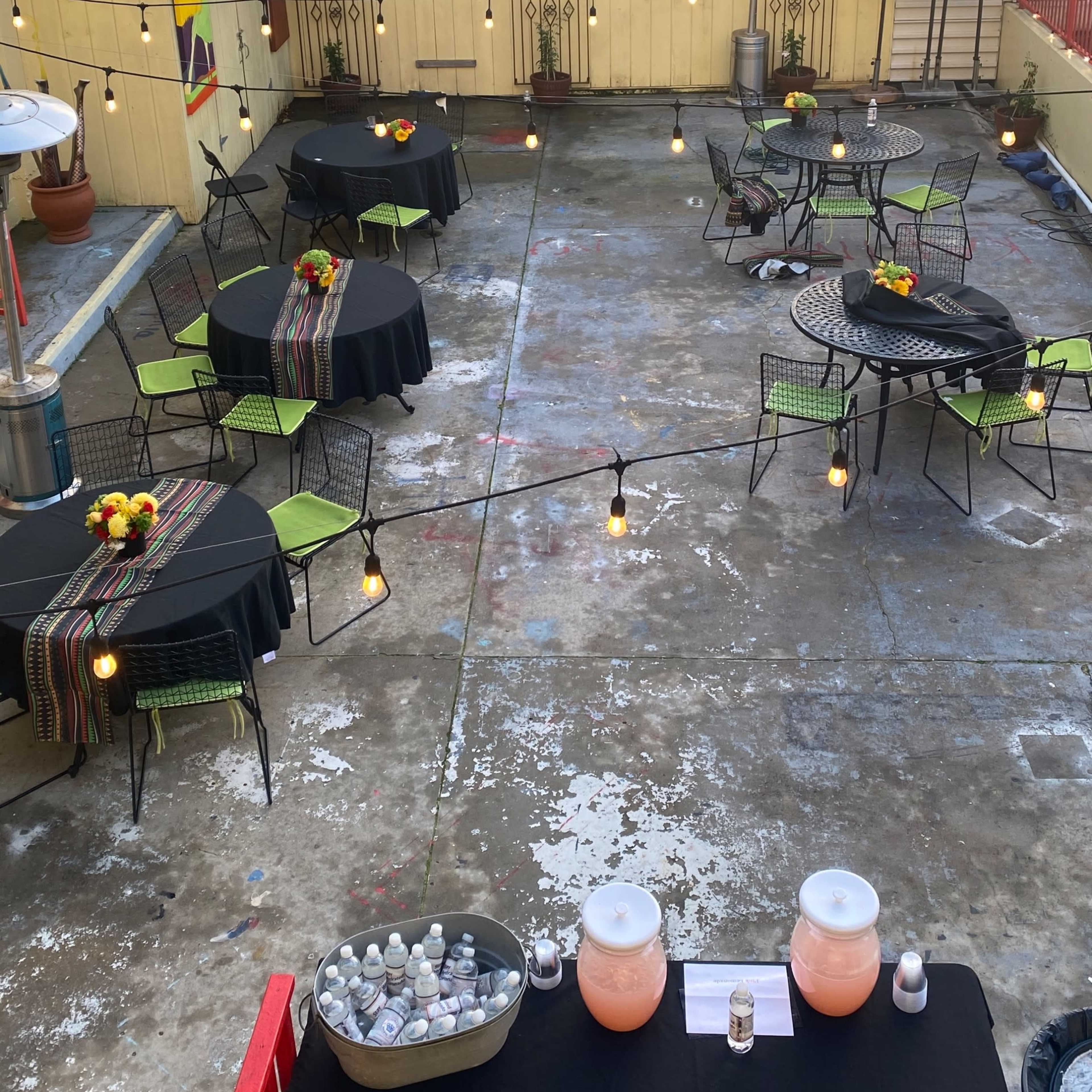 A rooftop space is set up with tables covered in black tablecloths, adorned with flowers, and string lights overhead.