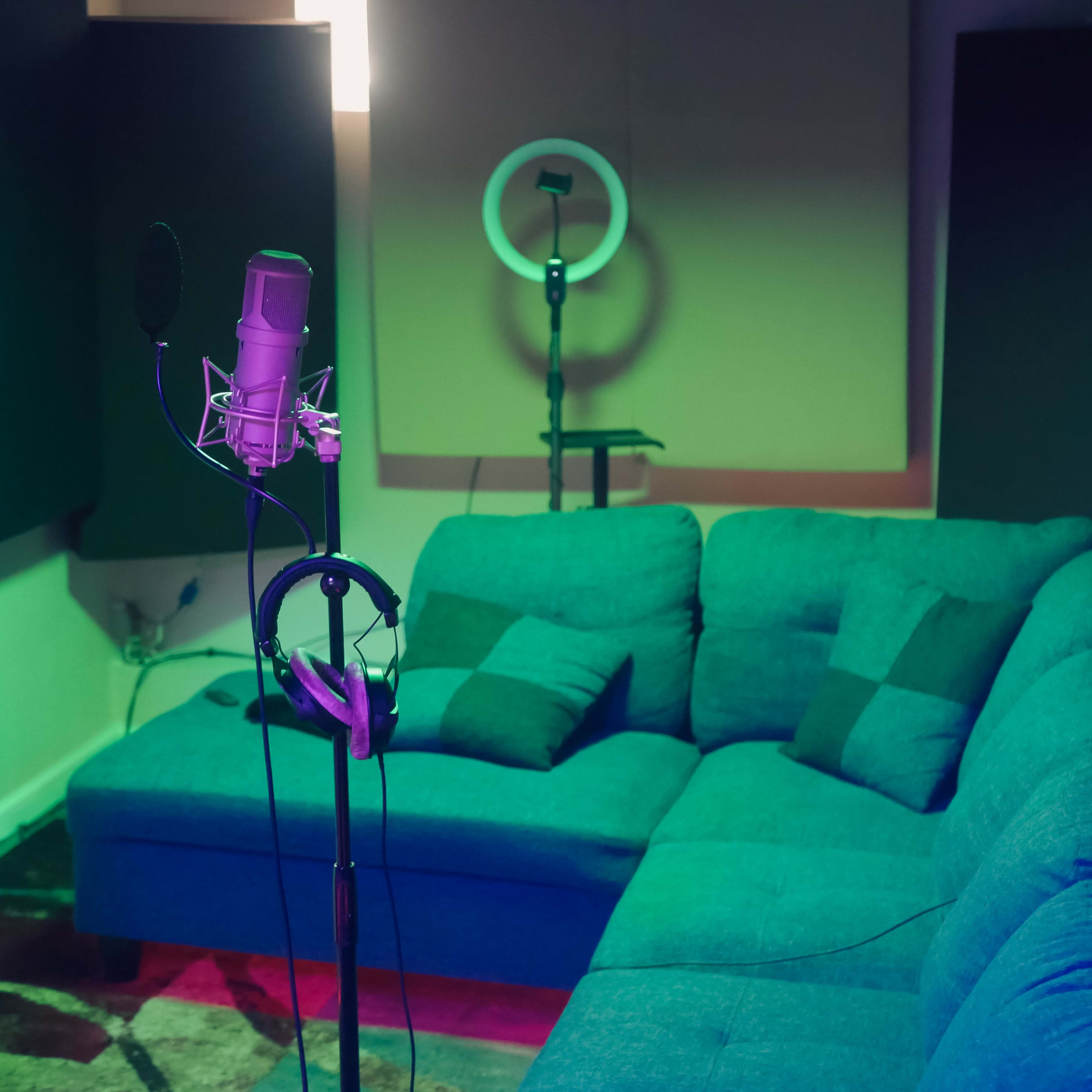 A recording studio with a microphone on a stand, headphones hanging nearby, and a couch in a dimly lit room.