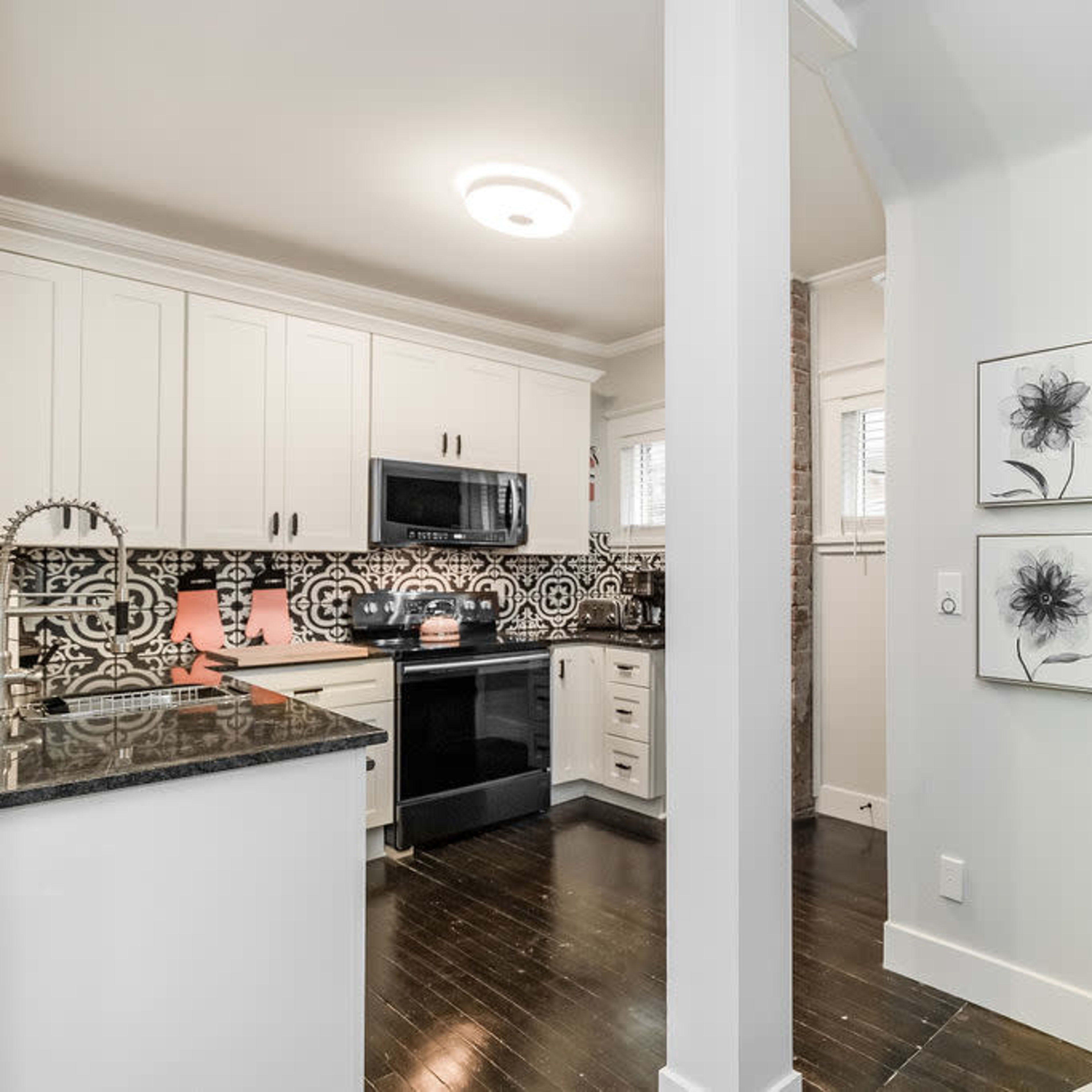 A modern kitchen with black and white tile backsplash, dark wood flooring, and a staircase leading to an upper level.