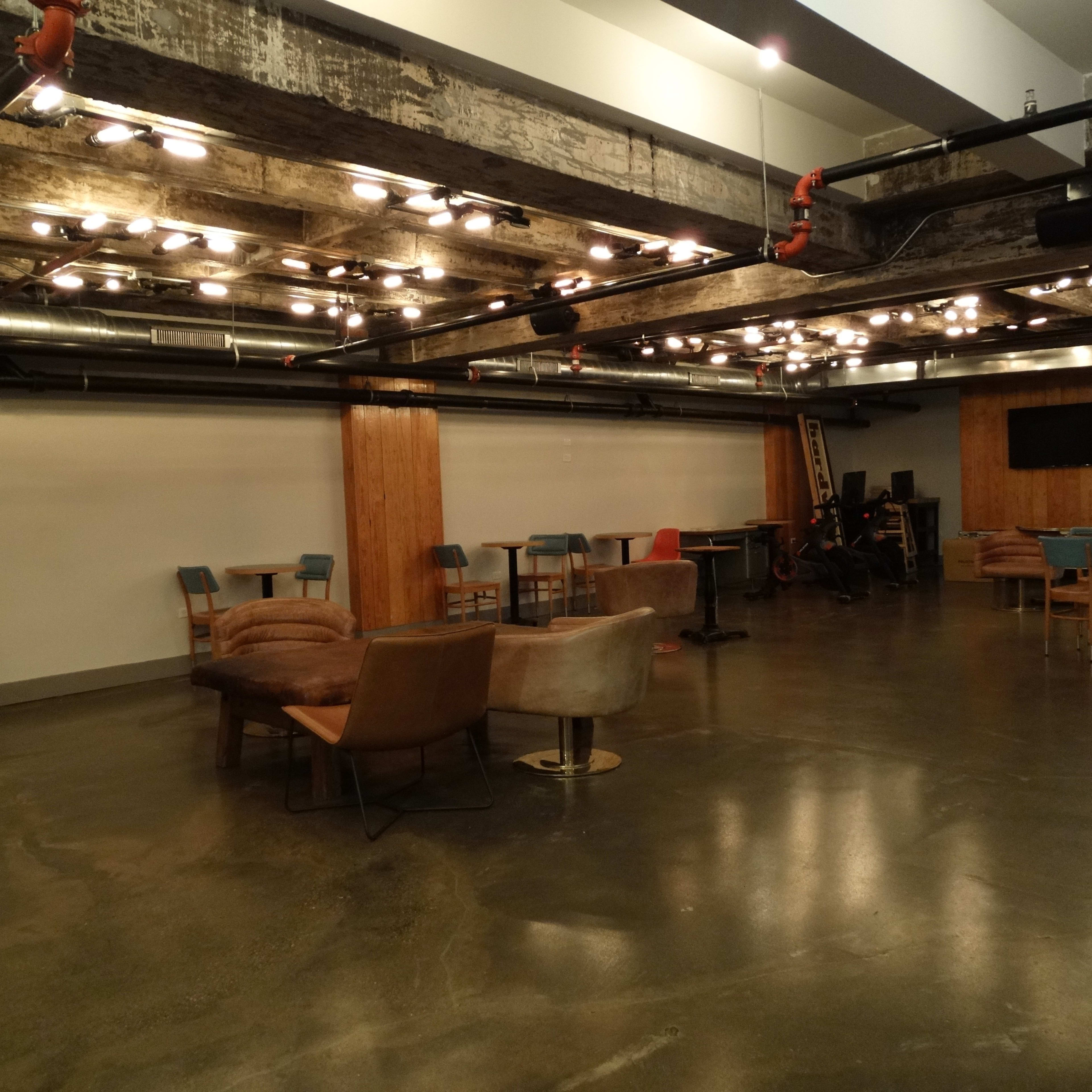 An empty, modern event space with various seating arrangements and exposed lighting fixtures.