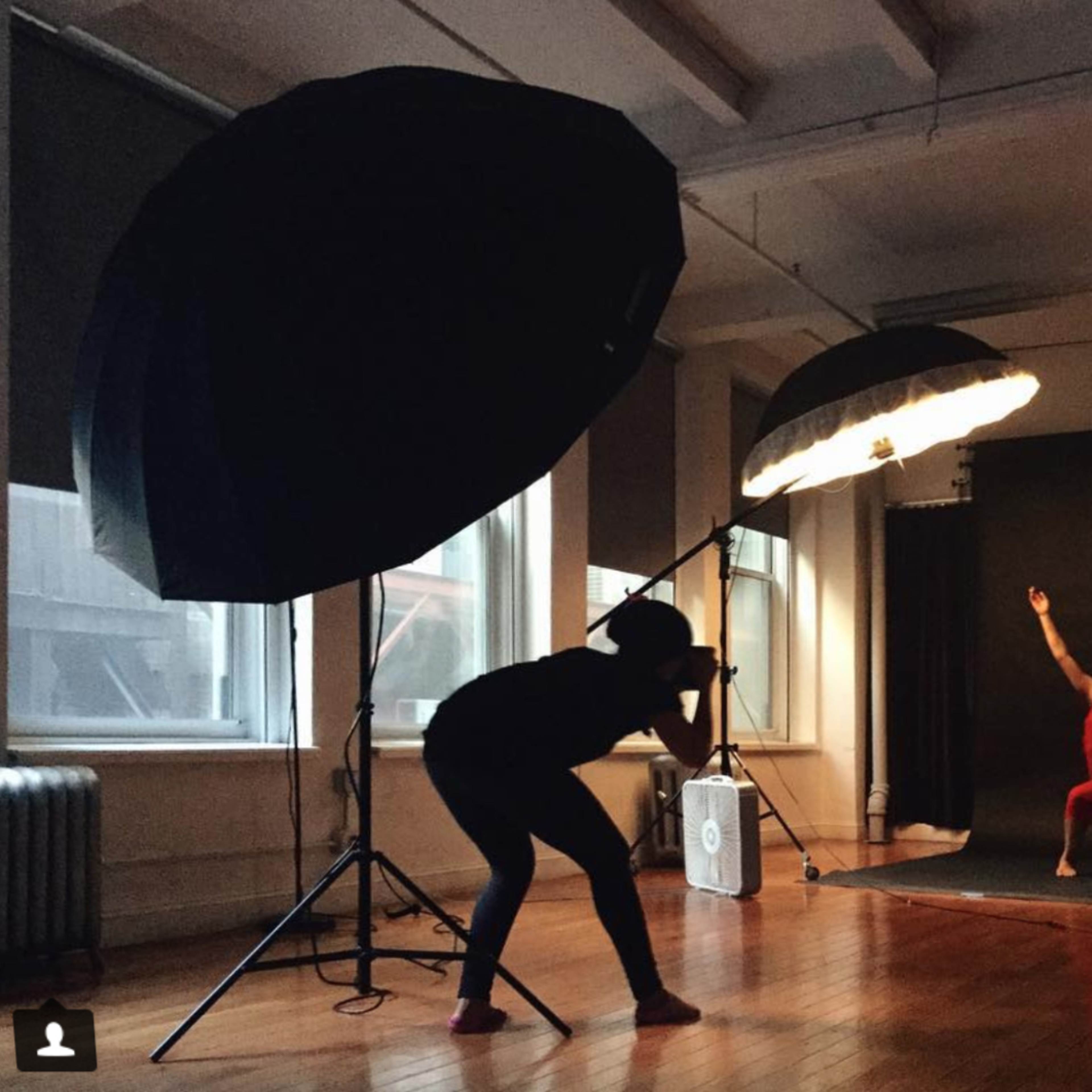 A photographer captures a dancer in a red dress striking a pose in a studio illuminated by large softbox lights.