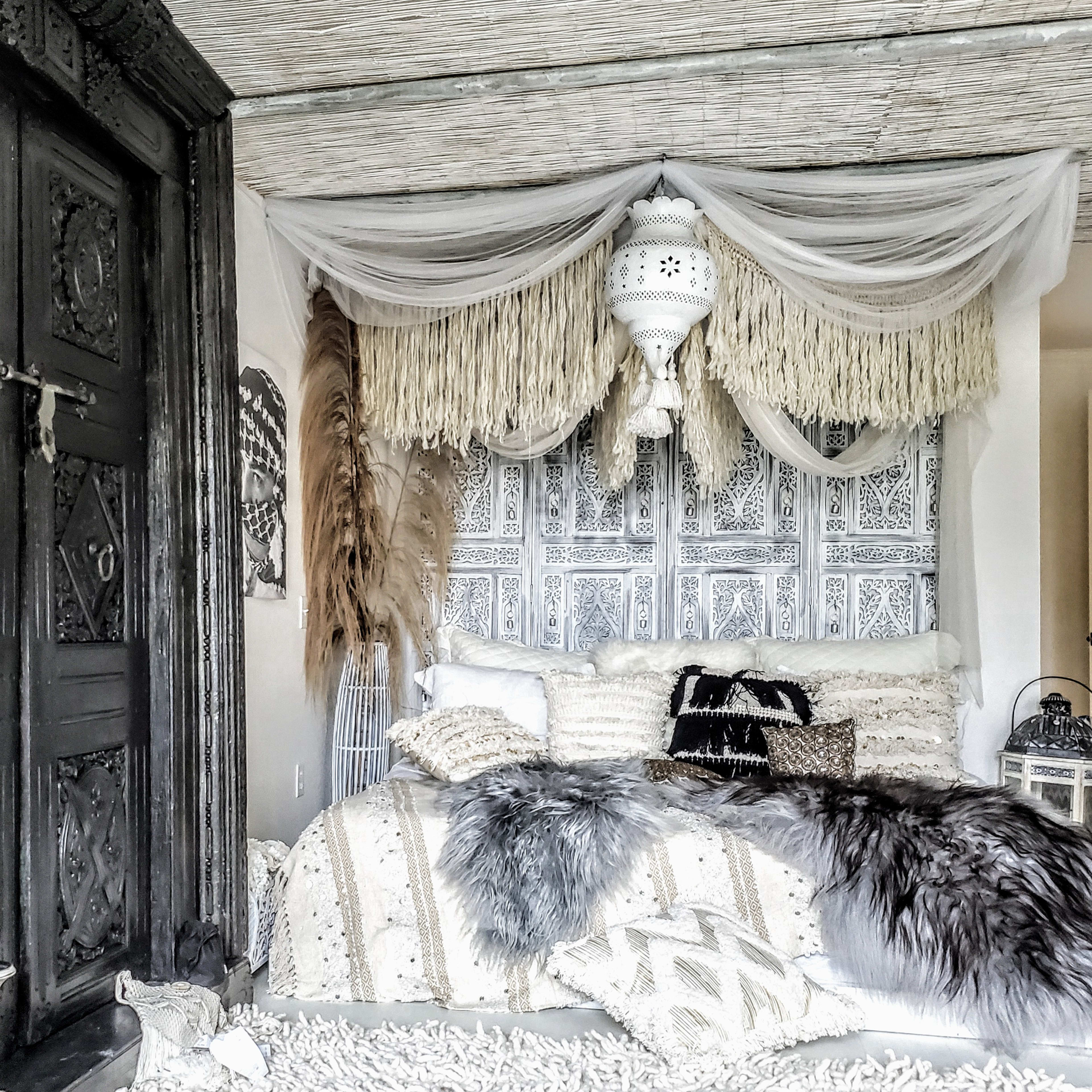 A stylish bedroom with a textured wall adorned with intricate designs, a bed covered in various decorative pillows and throws, and a lantern hanging above.