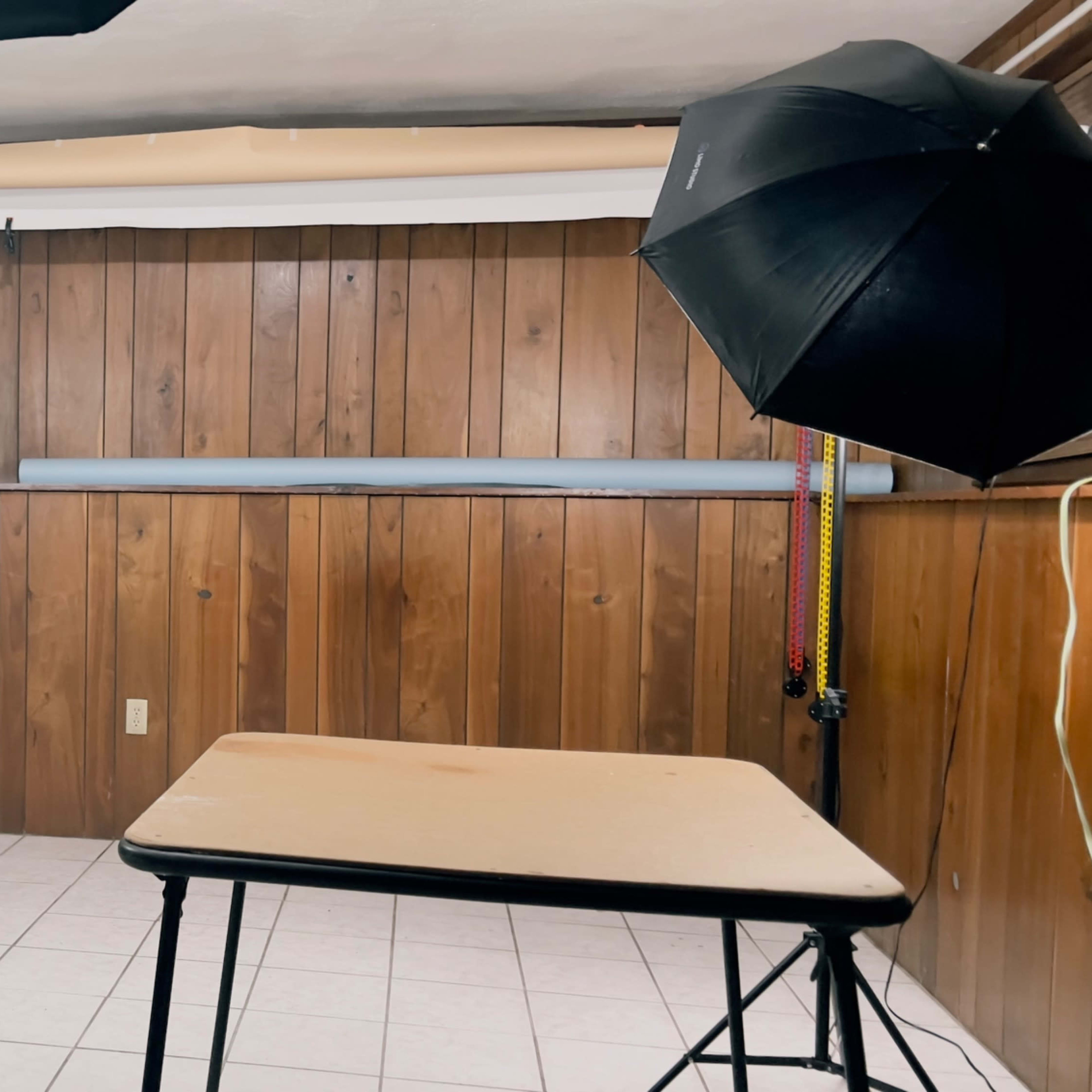 A photography setup in a room with wooden paneling, featuring a table in the center, studio lights on stands, and a fish tank in the corner.