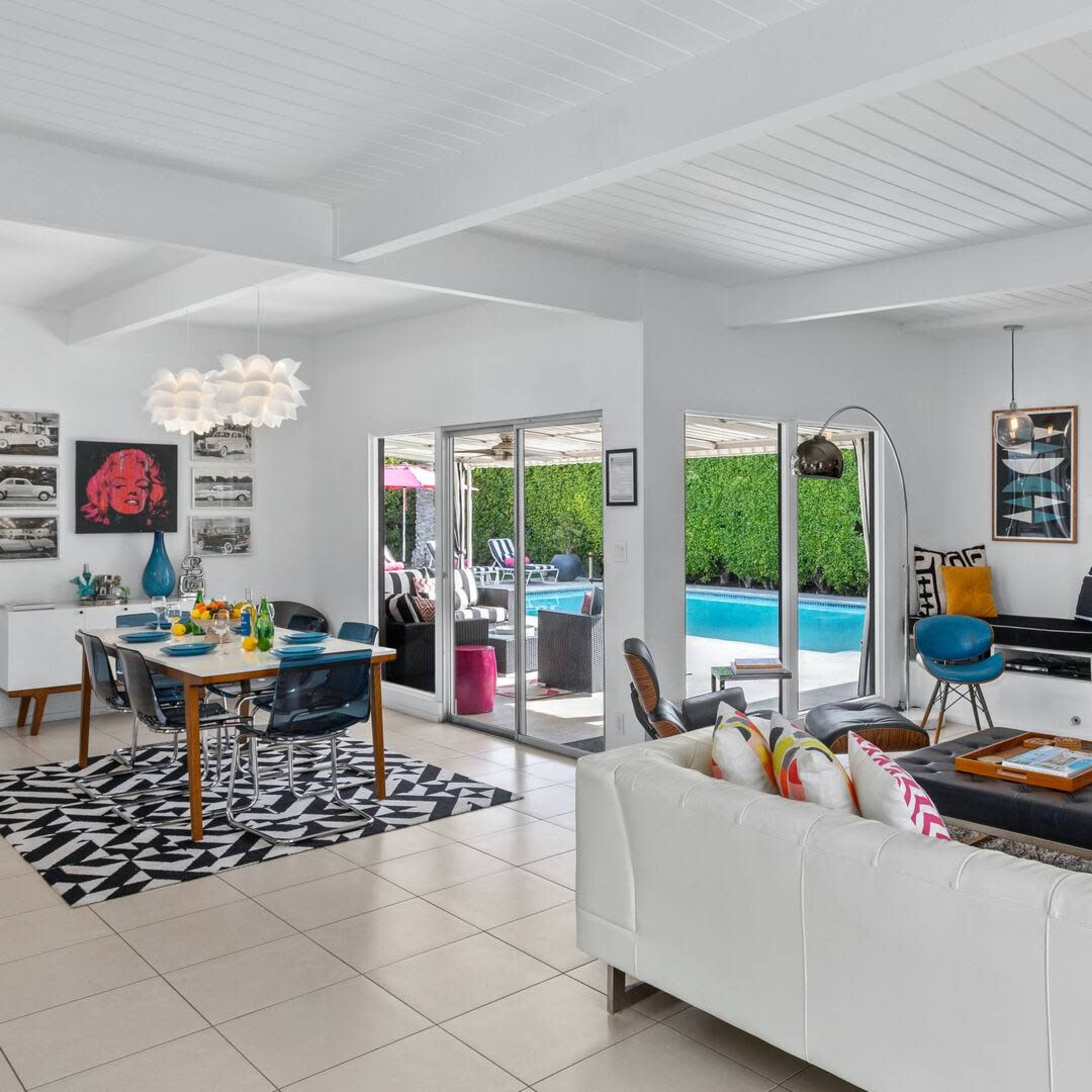 A modern living space featuring a white sofa, a dining area, a fireplace, and large sliding doors leading to a poolside patio.