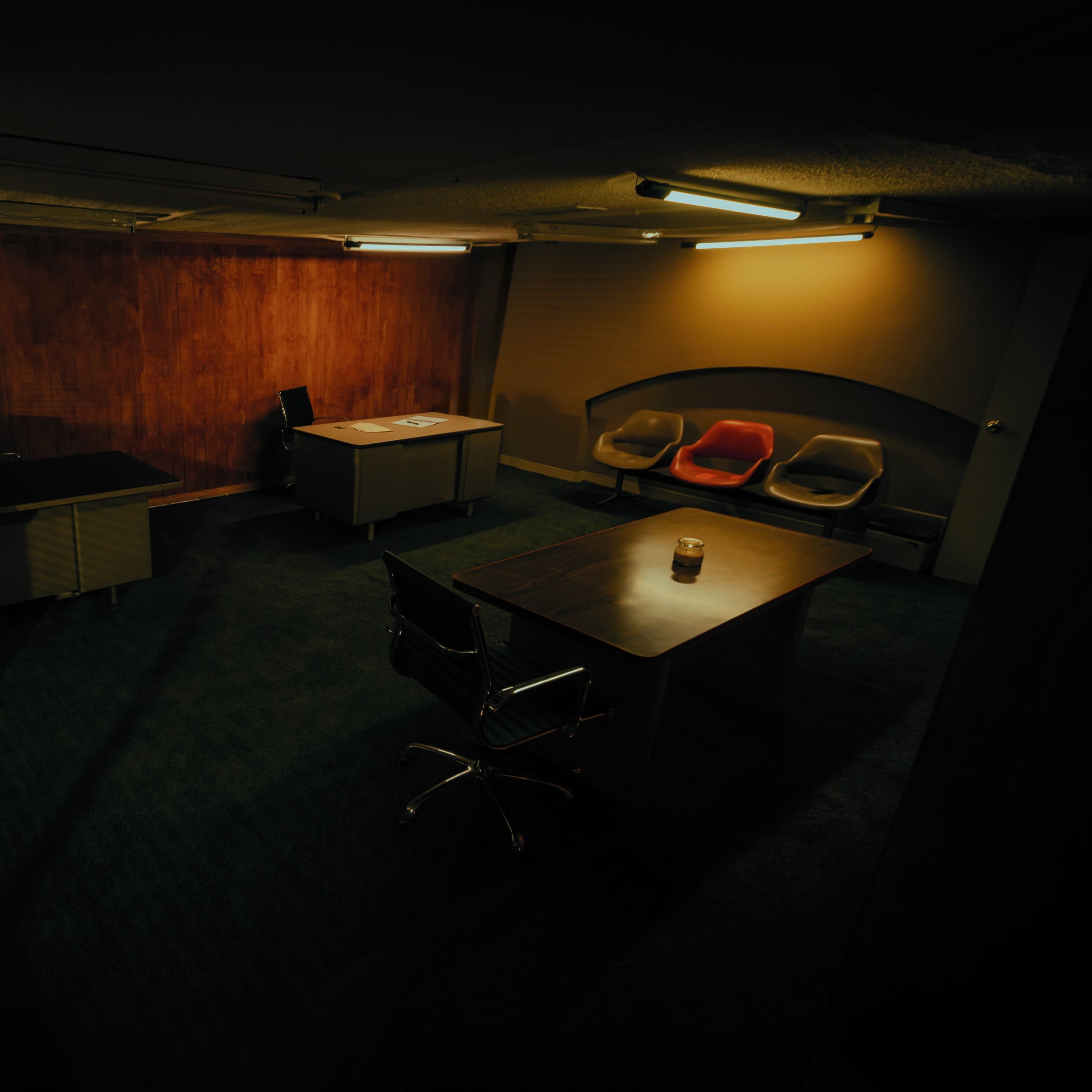 A dimly lit office space featuring two desks, a lamp, and a set of chairs.
