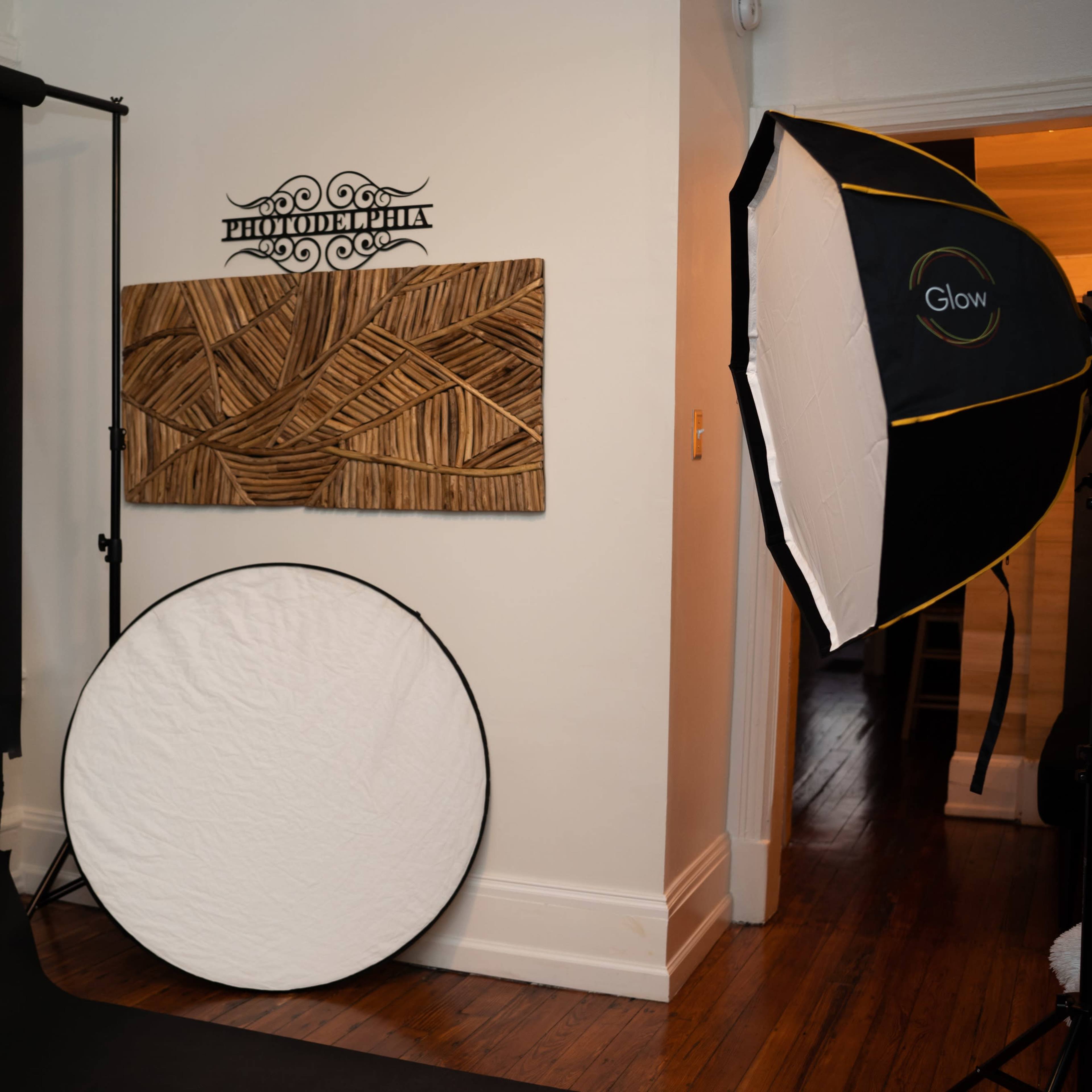 A photography studio setup with a black backdrop, a circular reflector on the floor, and a lighting umbrella positioned to the right.