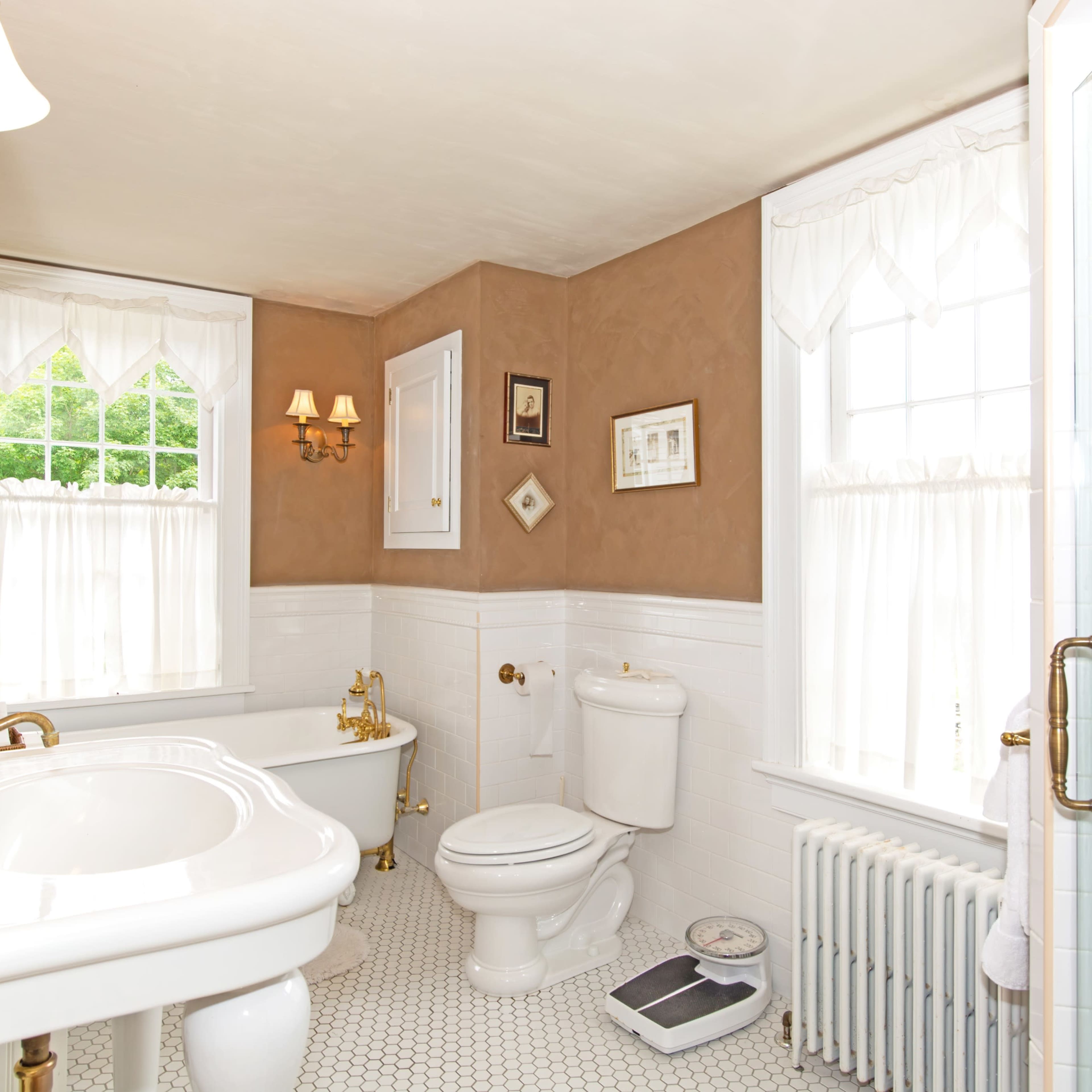 A bathroom featuring a clawfoot tub, white tile accents, a toilet, a sink with a decorative mirror above it, and a shower area with glass doors.