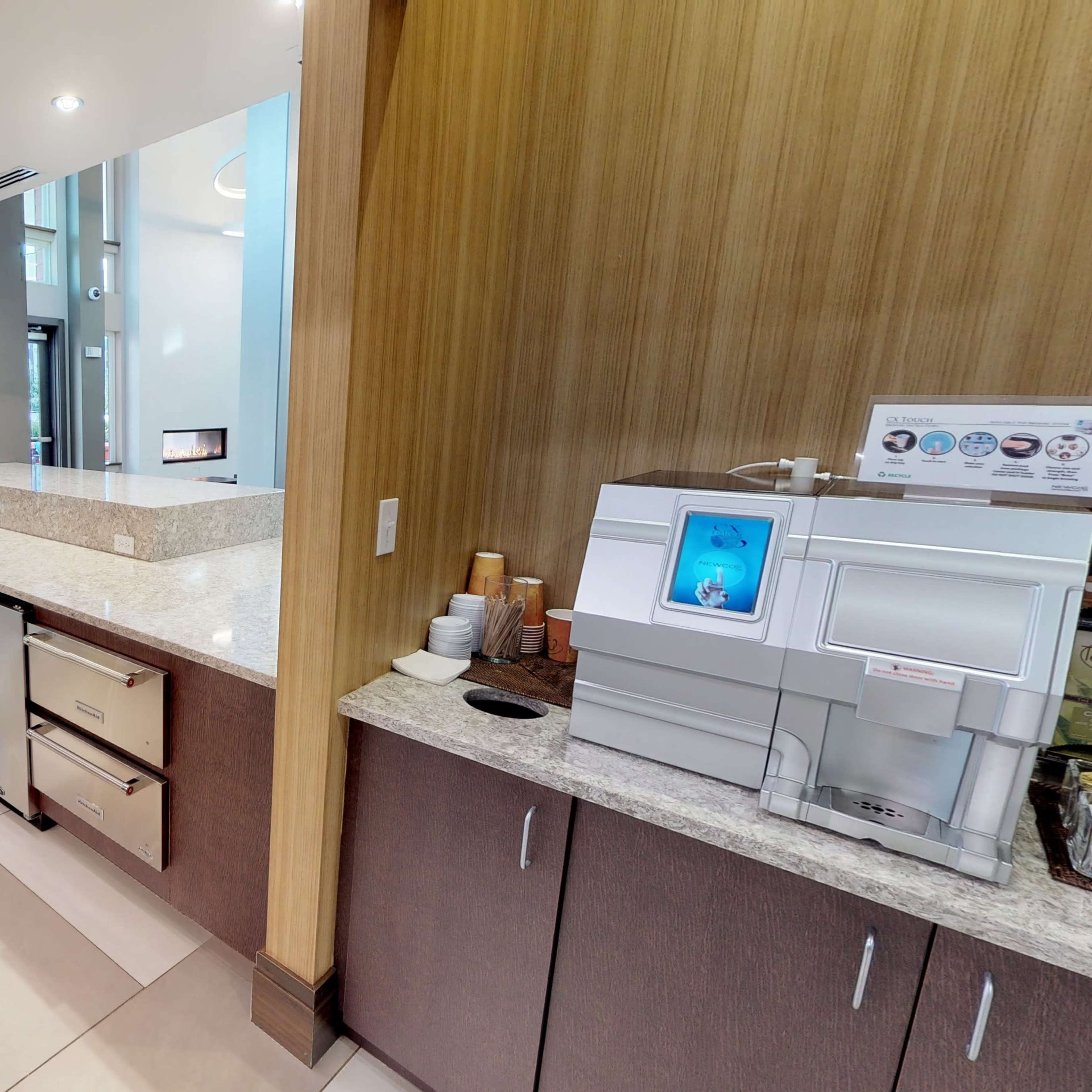 A modern kitchen area with granite countertops, a coffee machine, and a seating area visible in the background.