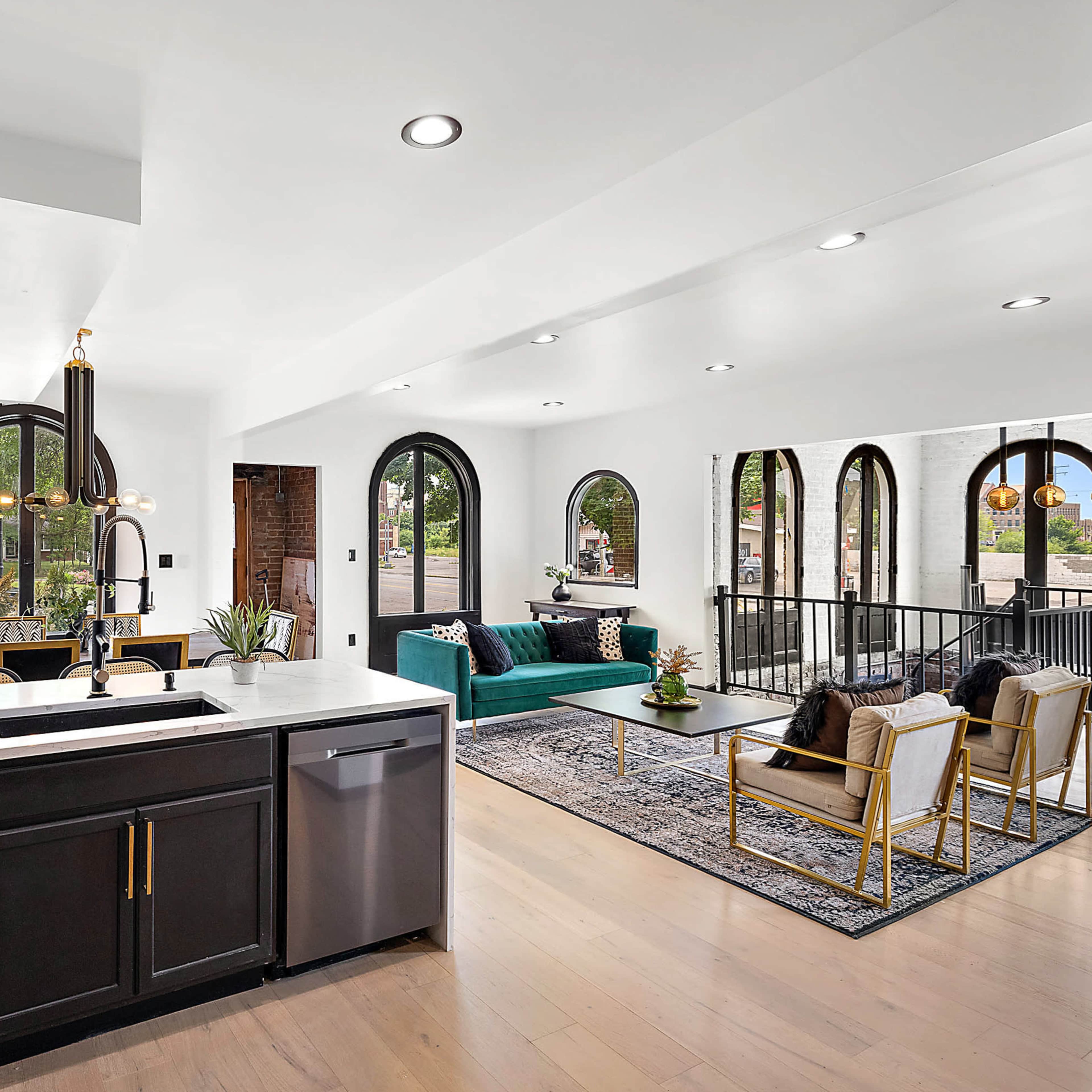 A modern kitchen with a black island, white countertops, and open living space featuring arched windows and a green sofa.