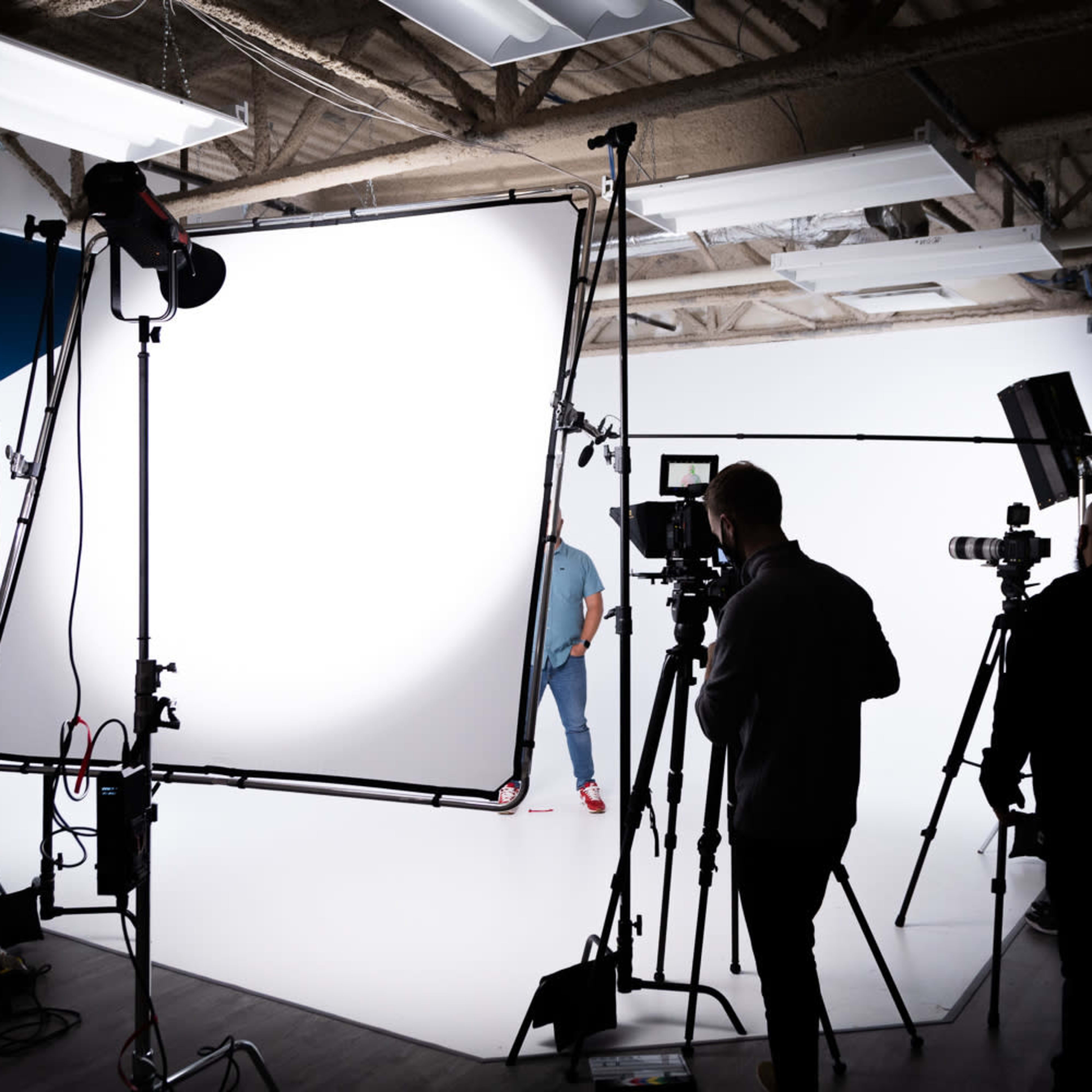 A photography studio is set up with multiple light sources and camera equipment focused on a person in front of a white backdrop.