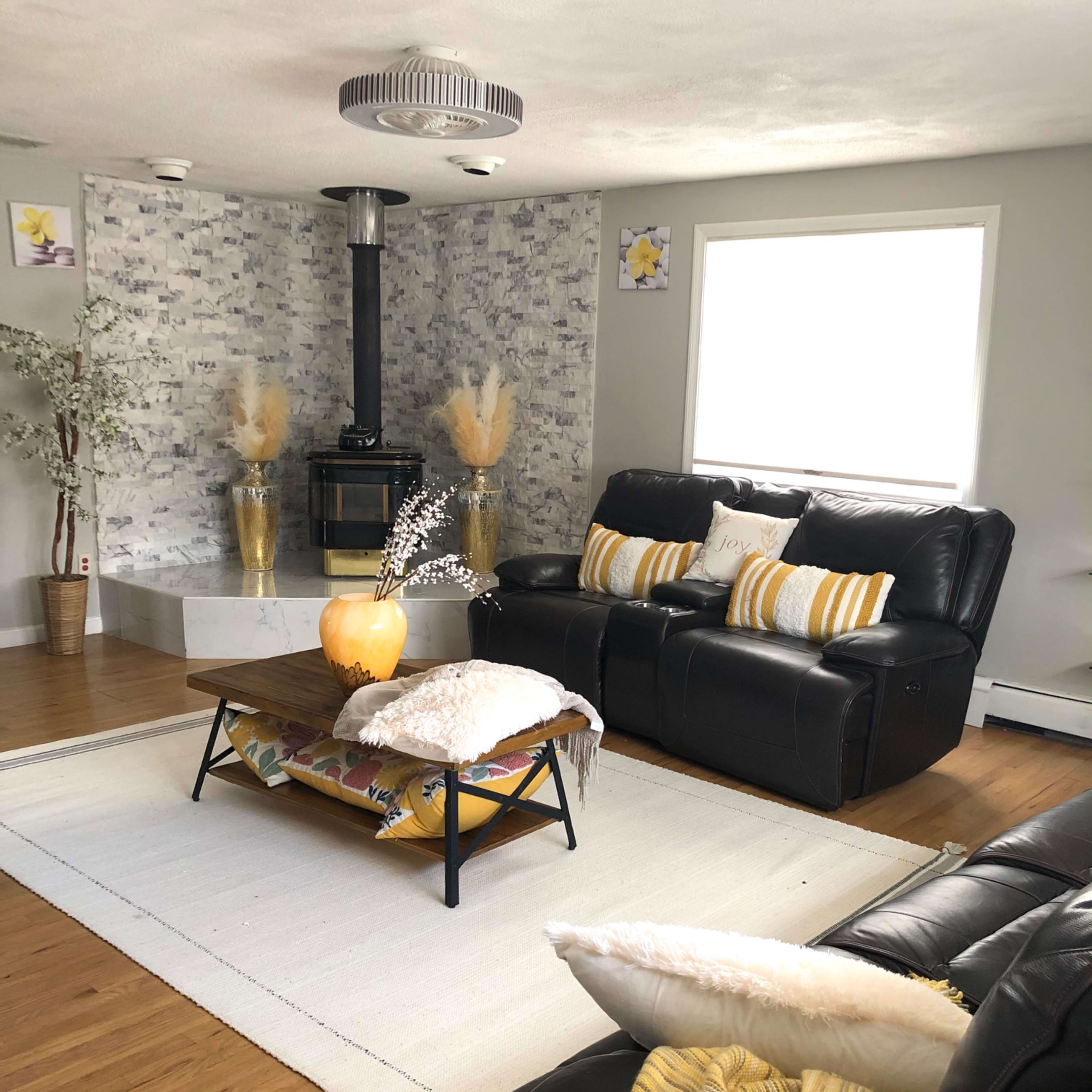 The living room features two black leather sofas facing a central coffee table, with a stone-clad fireplace in the background.