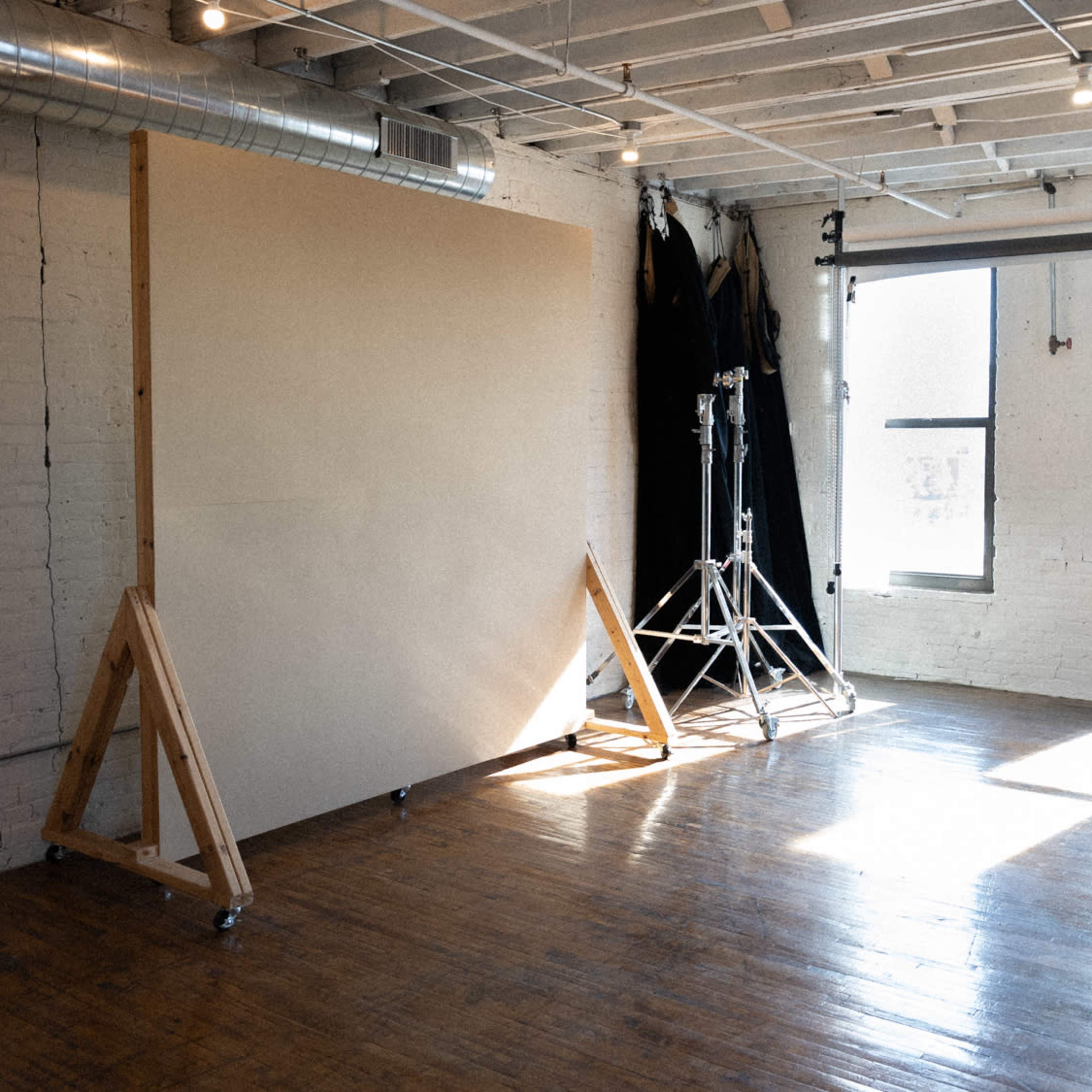 A spacious studio with a large wooden backdrop stand and soft natural light streaming through the windows.