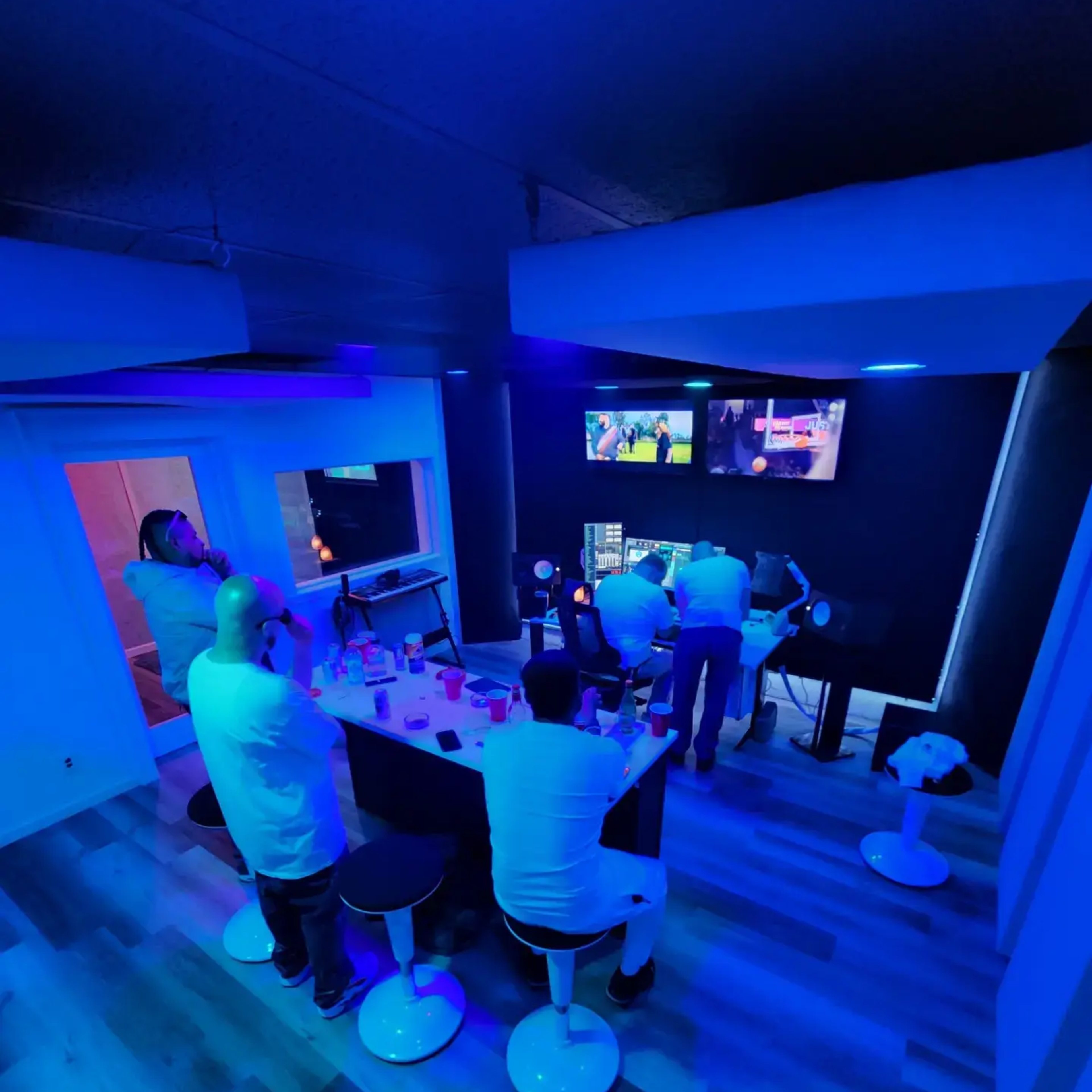 A modern recording studio with a long counter, a large desk equipped with audio equipment, and blue ambient lighting.