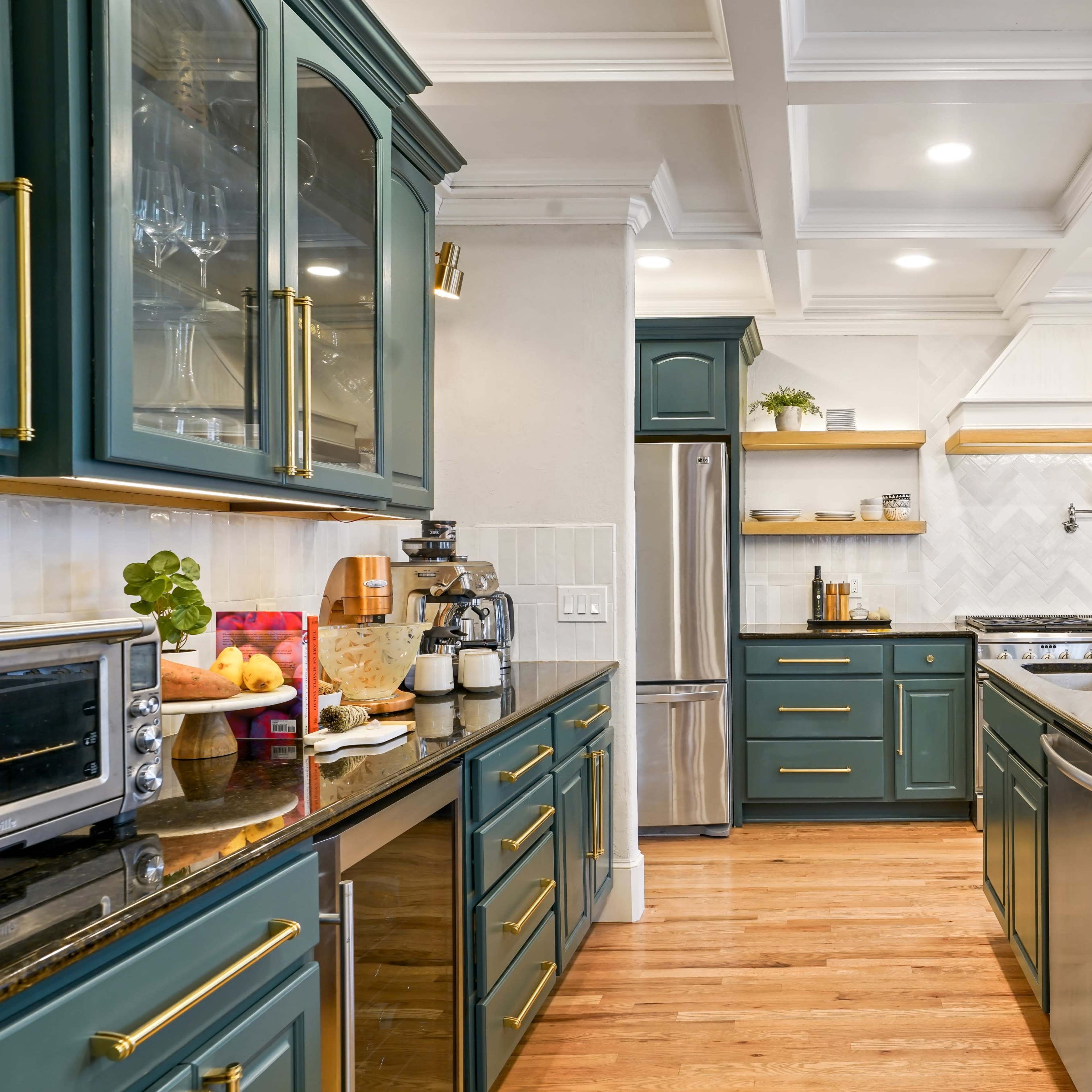 A modern kitchen features green cabinetry, stainless steel appliances, and a large island with a dark countertop.