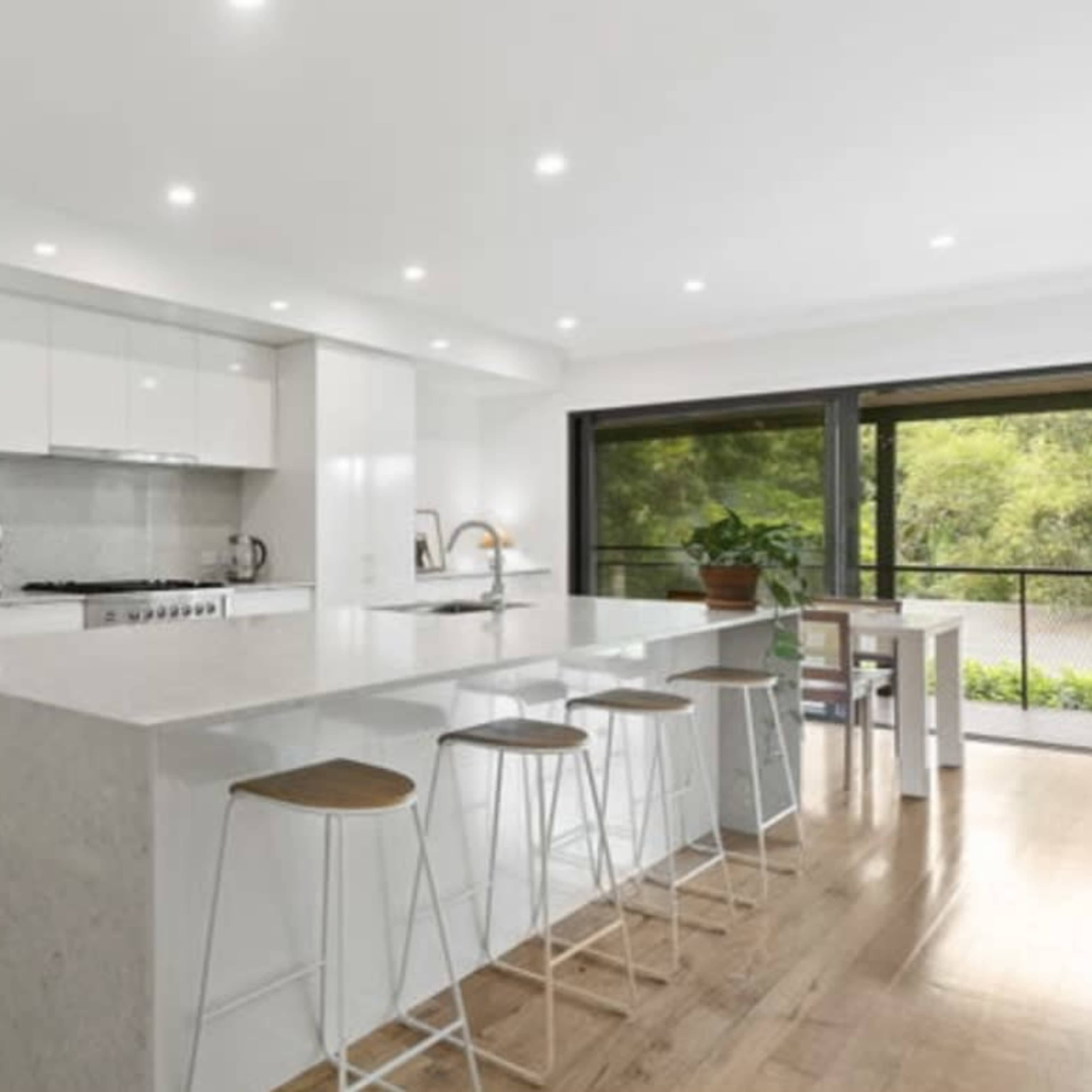 A modern kitchen with white cabinetry, a large island with bar stools, and a window overlooking a green area.