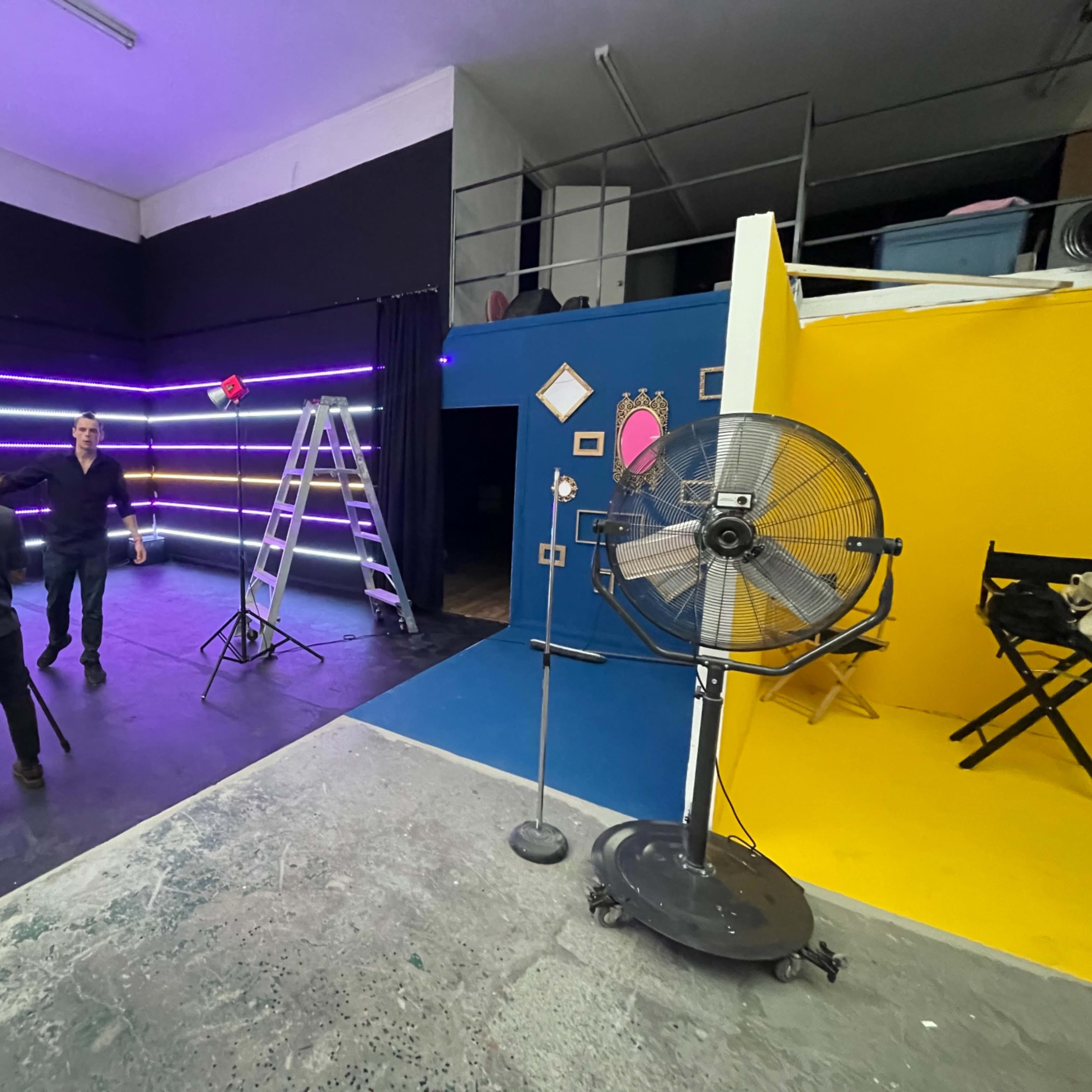 A photography studio features a mix of props, lighting equipment, and colorful backdrops, with individuals preparing for a shoot.
