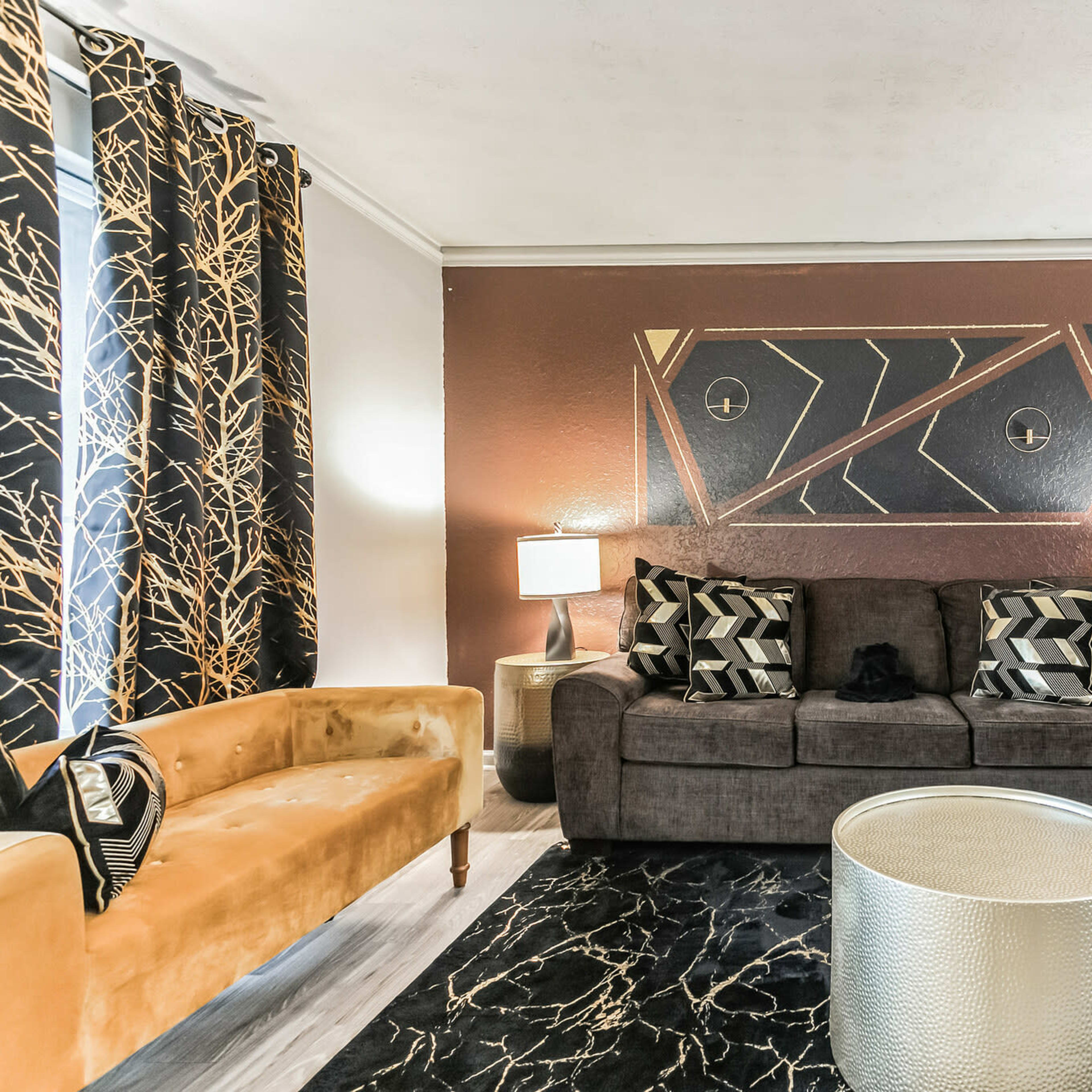 A living room with a dark sofa, a gold-colored coffee table, and decorative curtains featuring a tree branch pattern.