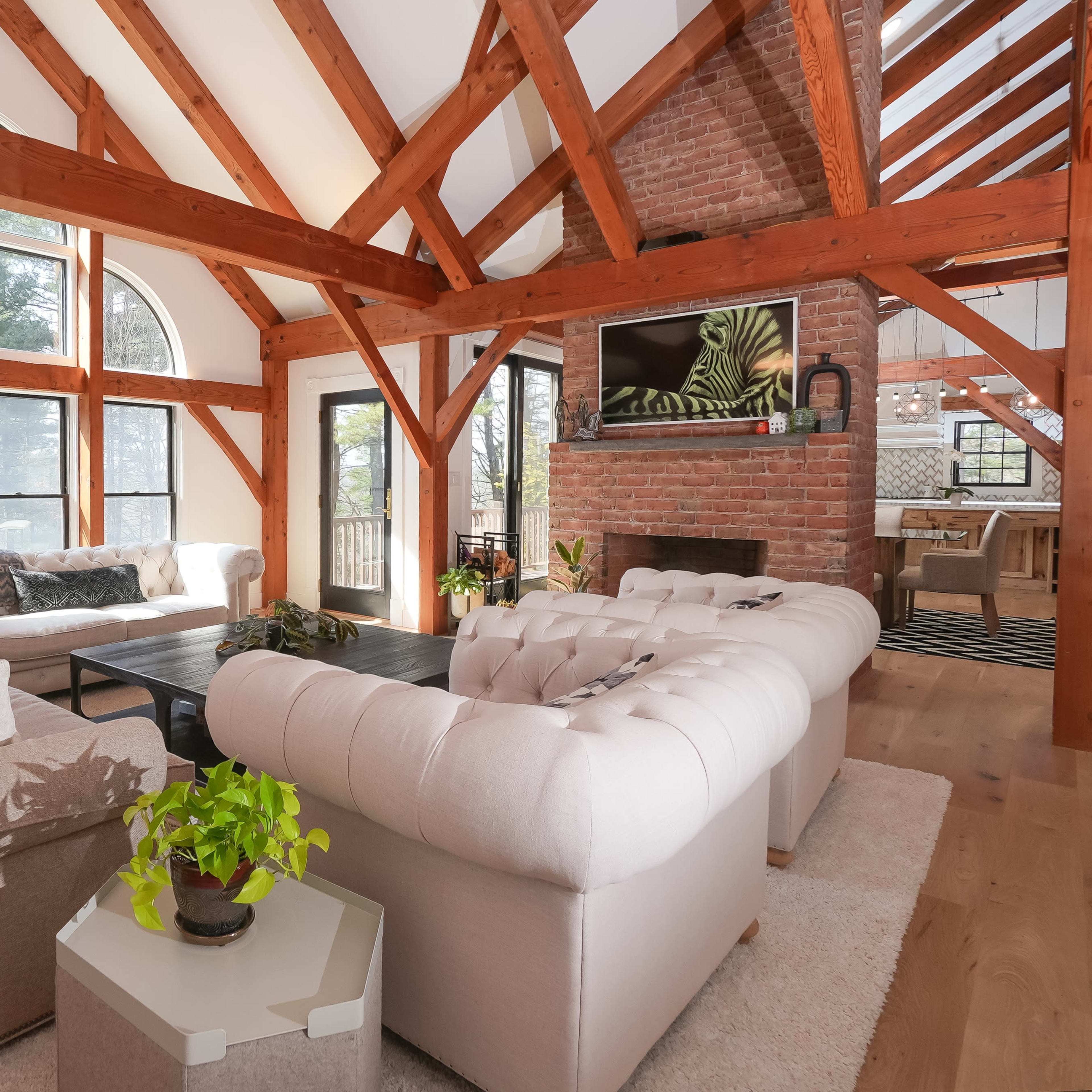 A spacious living room with wooden beams, large windows, and two upholstered sofas arranged around a coffee table.
