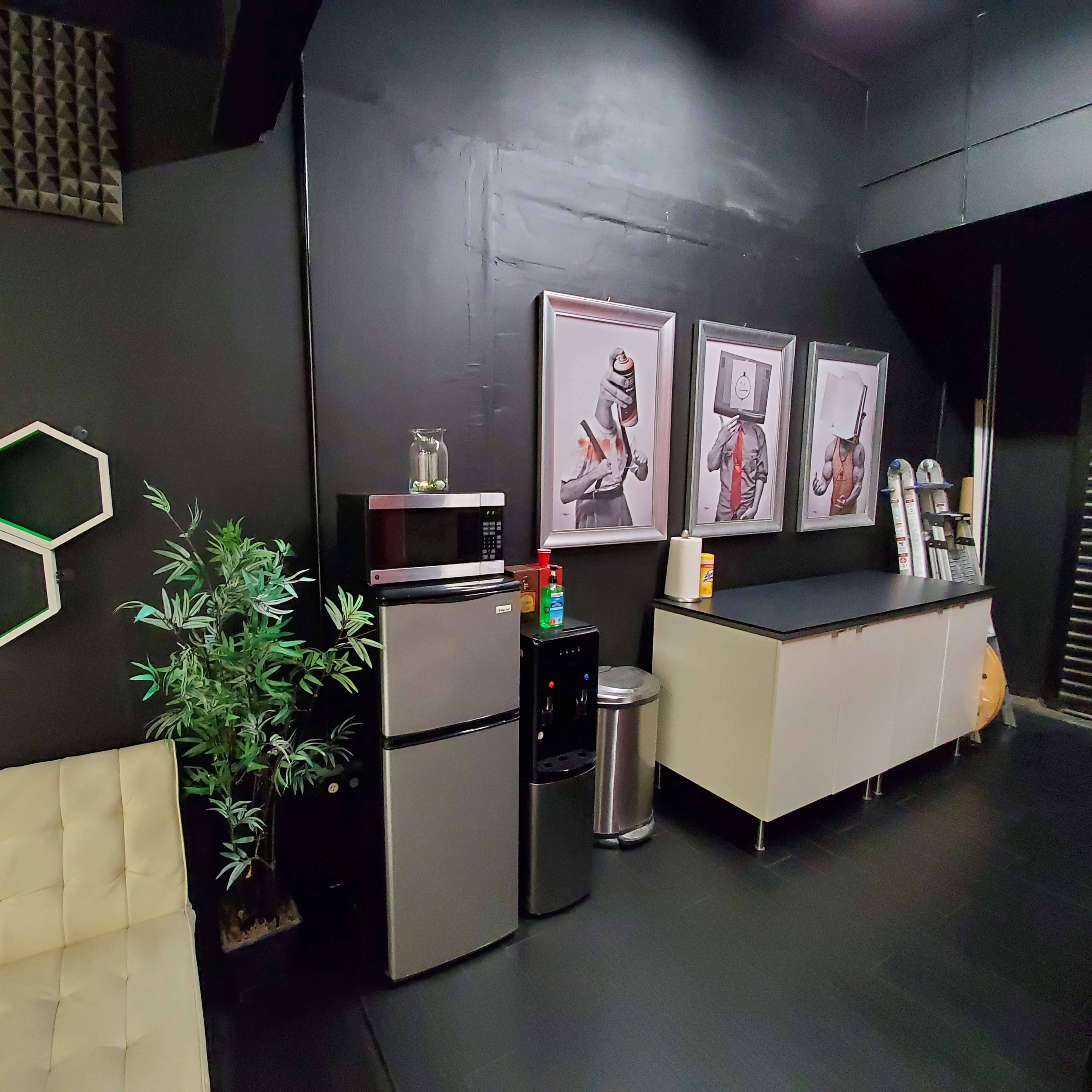 A darkly painted room featuring a seating area with a white couch, a kitchenette with a refrigerator, and framed artwork on the wall.