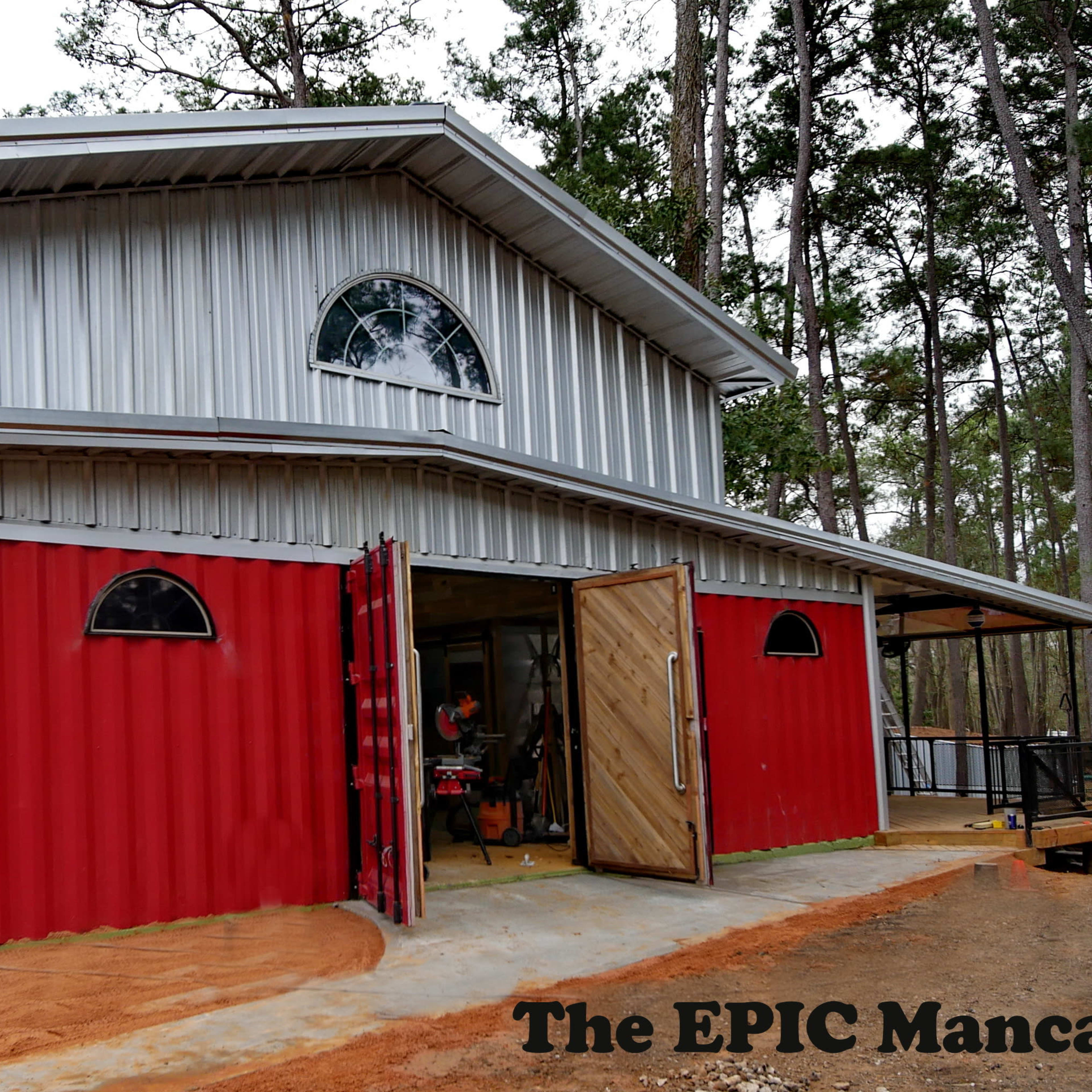 A modern, two-story building constructed with a metal roof and red shipping containers incorporated as walls, surrounded by trees.