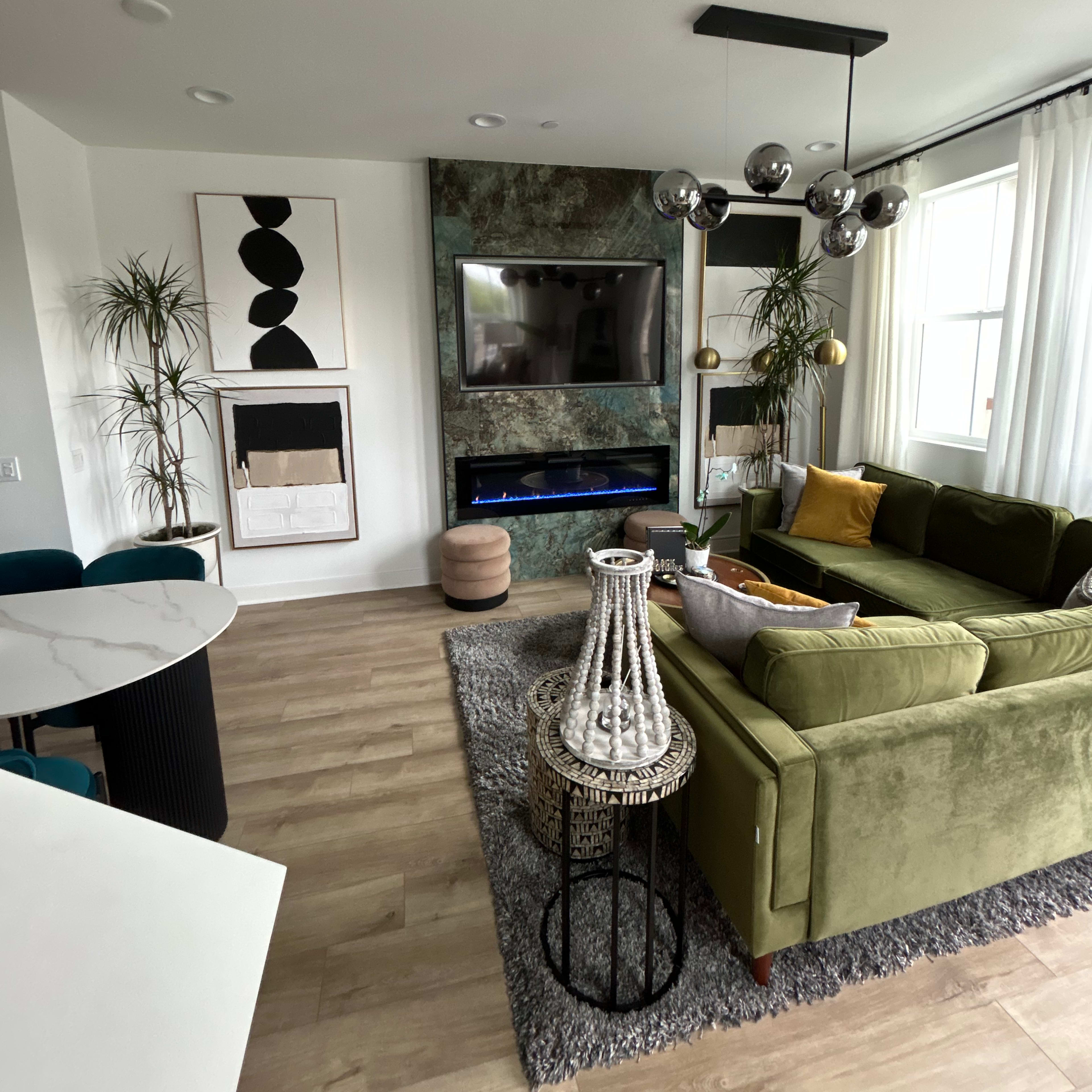 A modern living room with a green sofa, a round coffee table, a large wall-mounted TV, and various decorative plants.