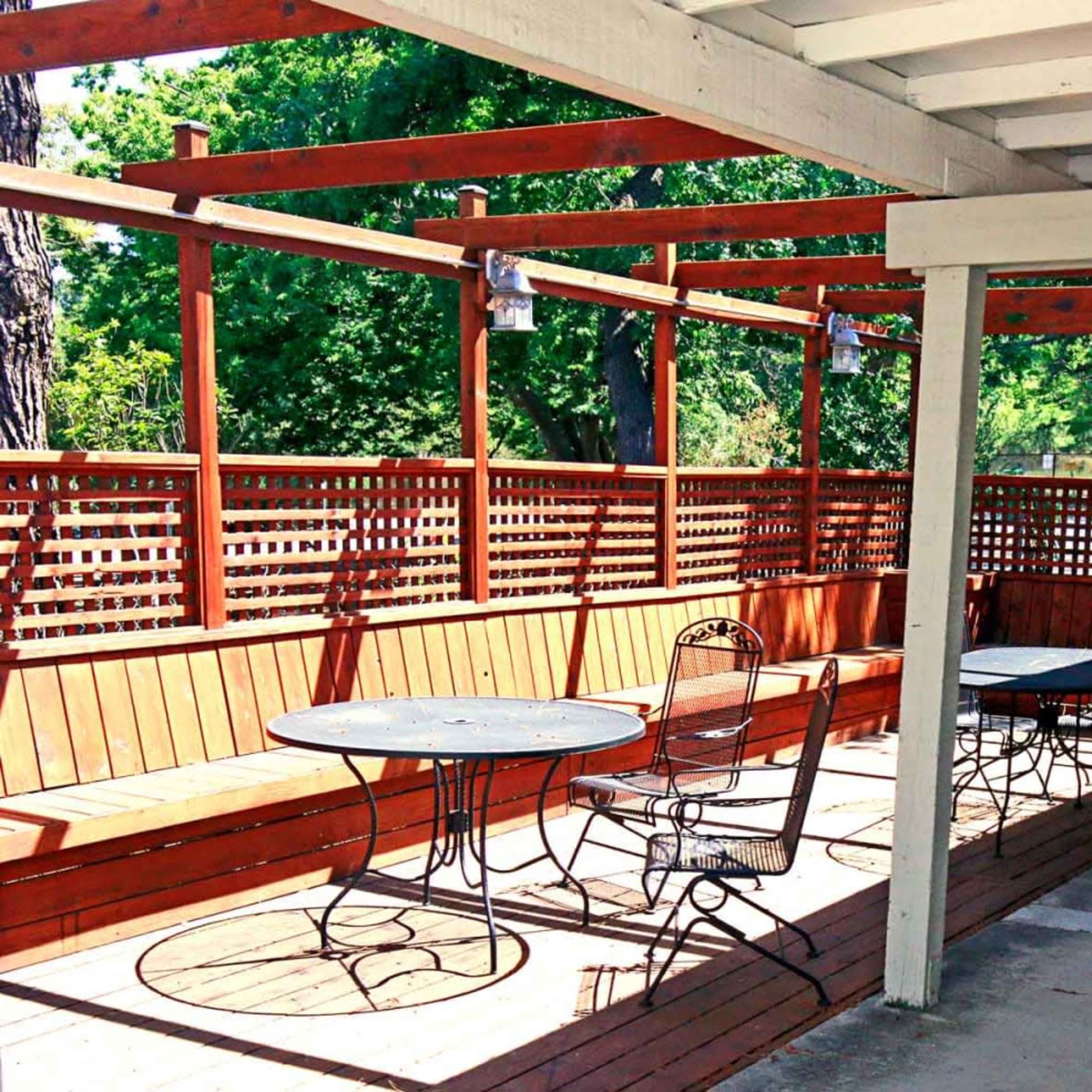 A patio area with wooden benches and tables, surrounded by a slatted wooden fence.