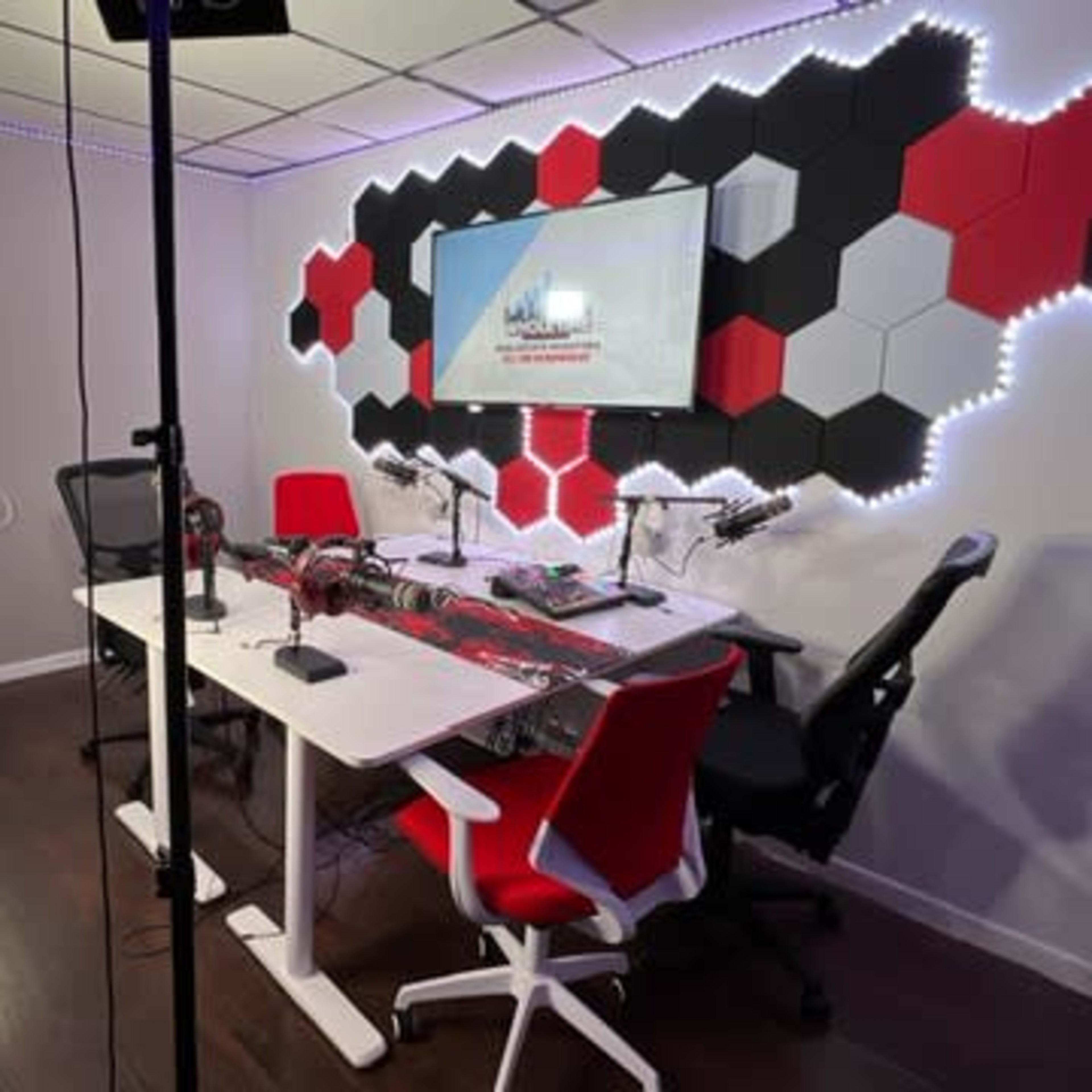 A modern recording studio with a hexagonal wall design, two desks, and professional lighting equipment.