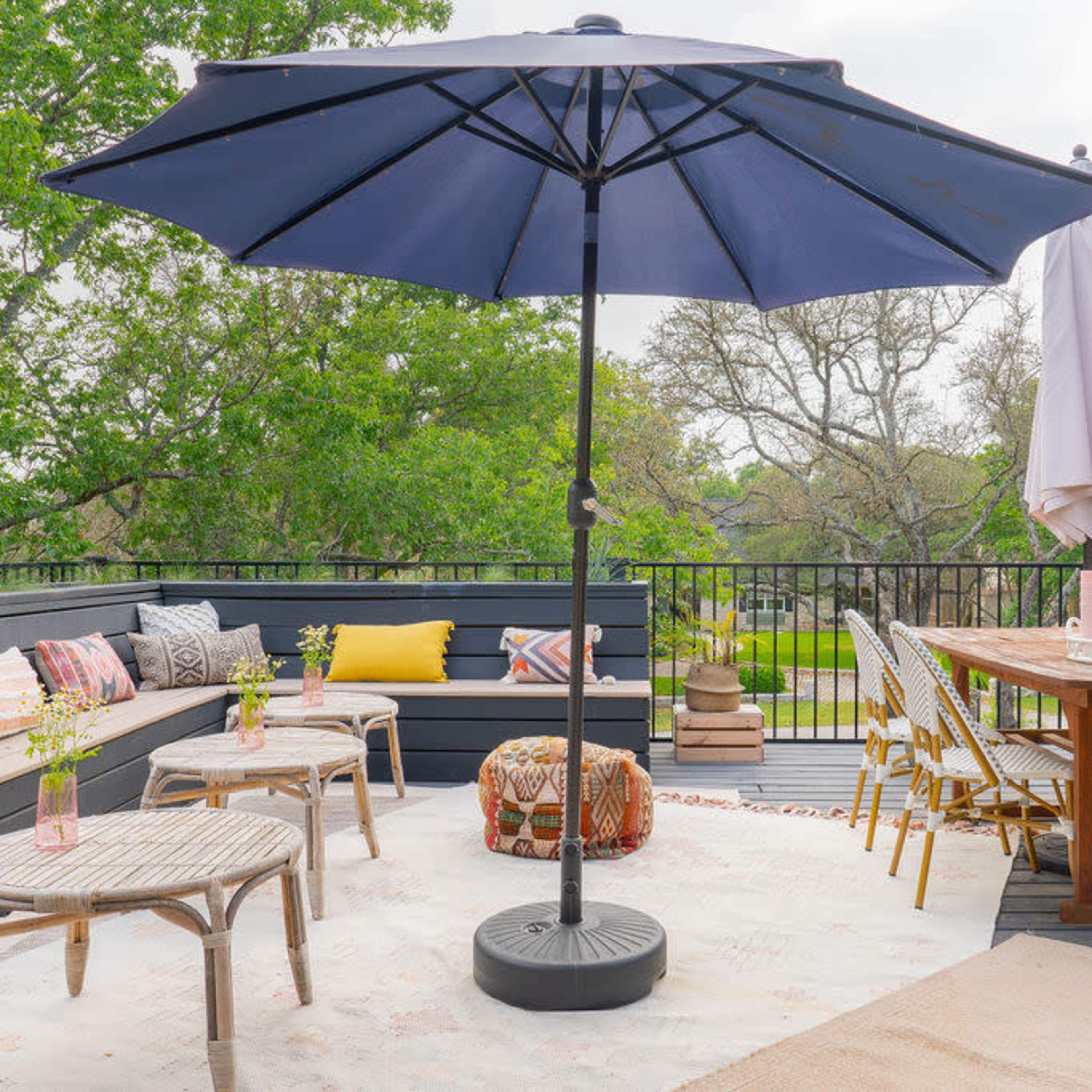 A patio with a seated area featuring a large umbrella, a dining table with chairs, and decorative pillows arranged around a rug.