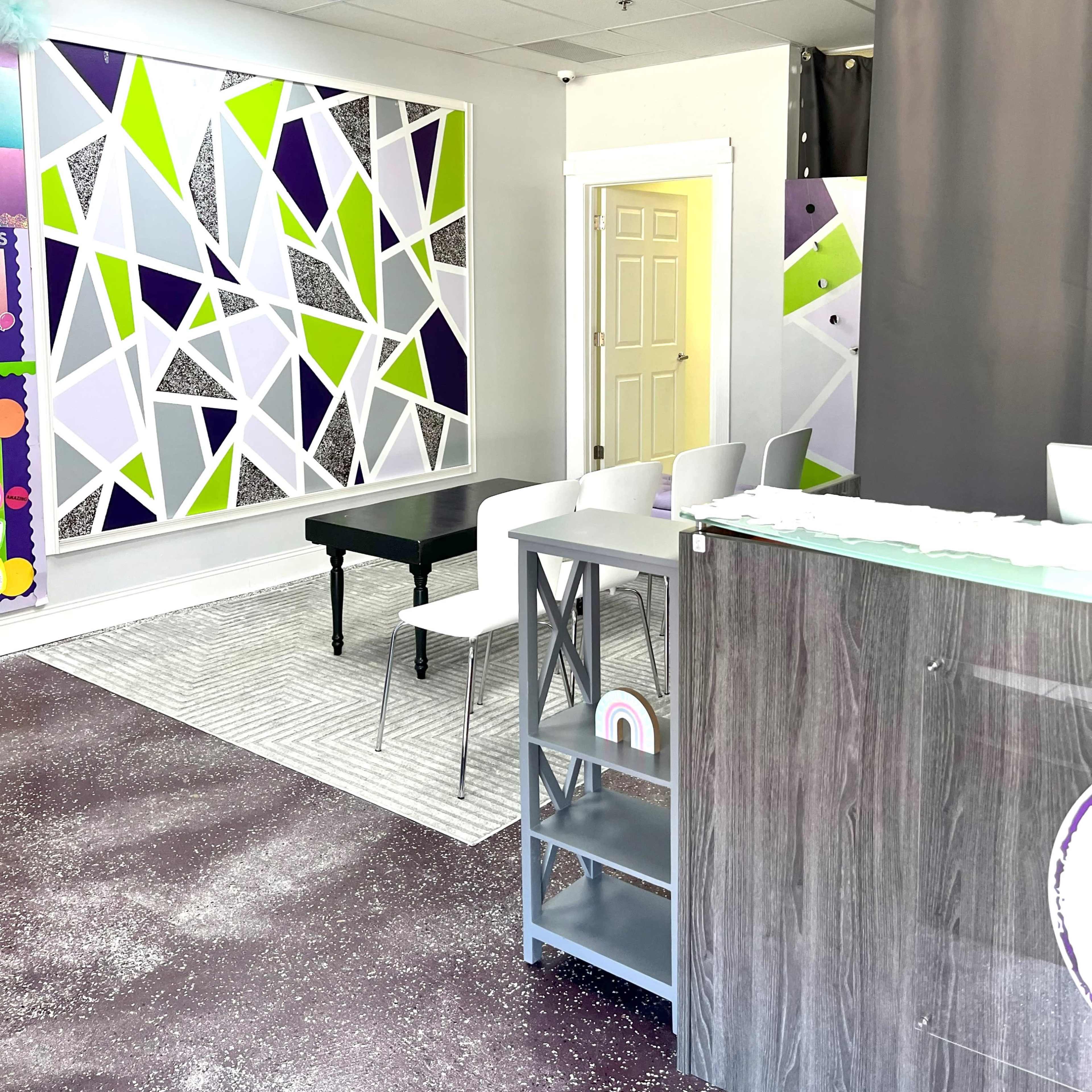 A brightly colored modern interior of a studio or office, featuring geometric wall art, a reception desk, and seating arrangements.