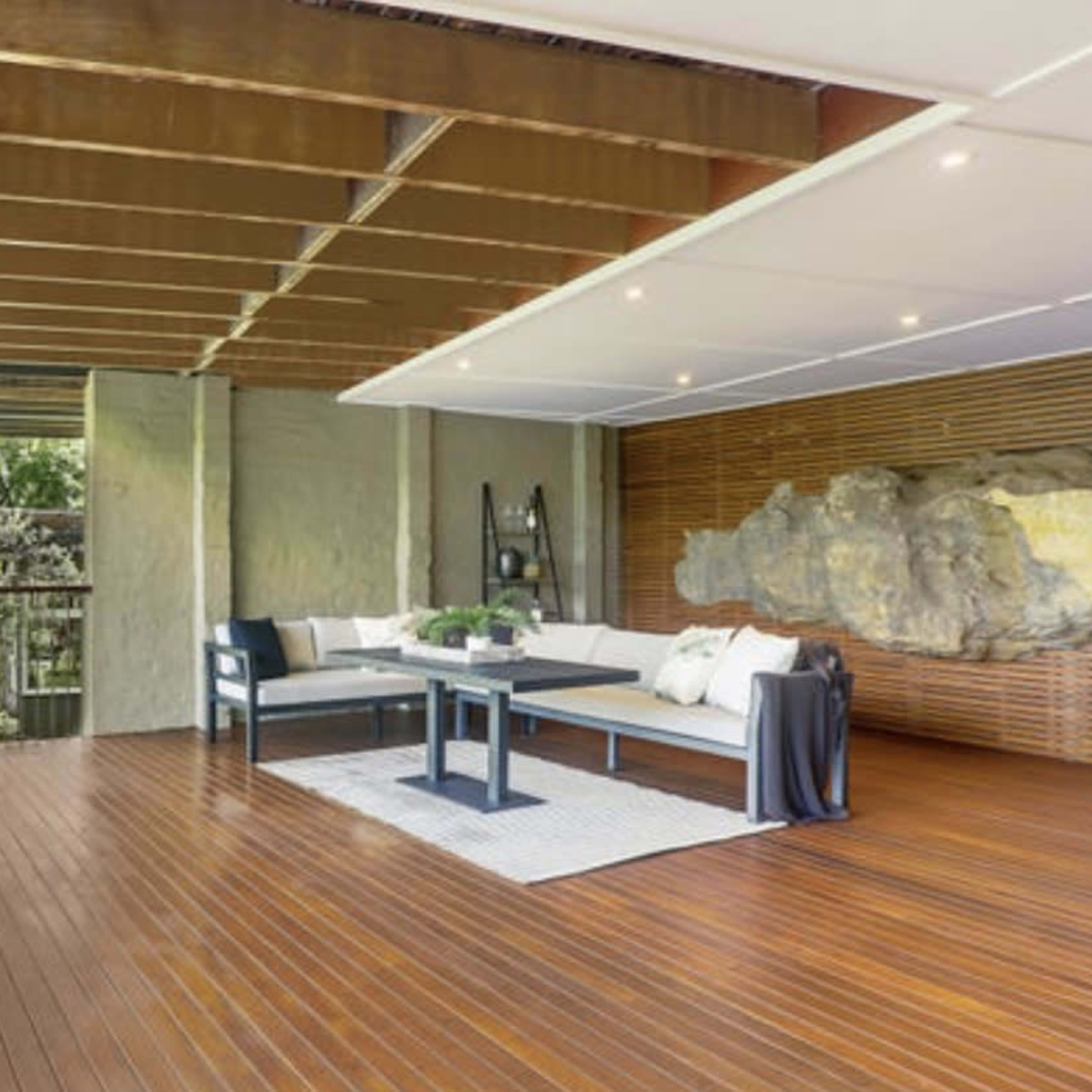 A spacious outdoor living area with wooden flooring, a modern seating arrangement, and greenery visible in the background.