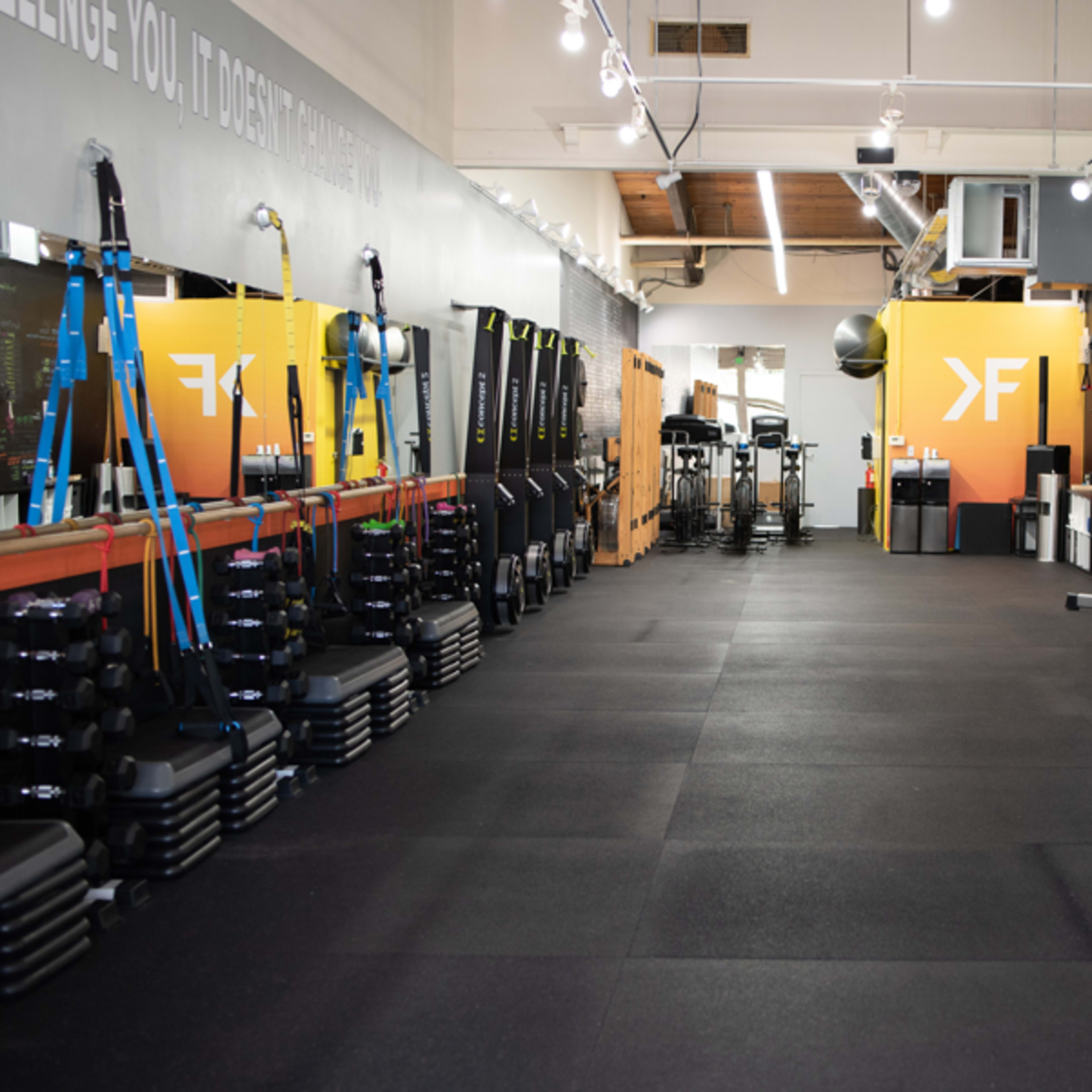 A gym interior with various exercise equipment organized along the walls and an open central area.