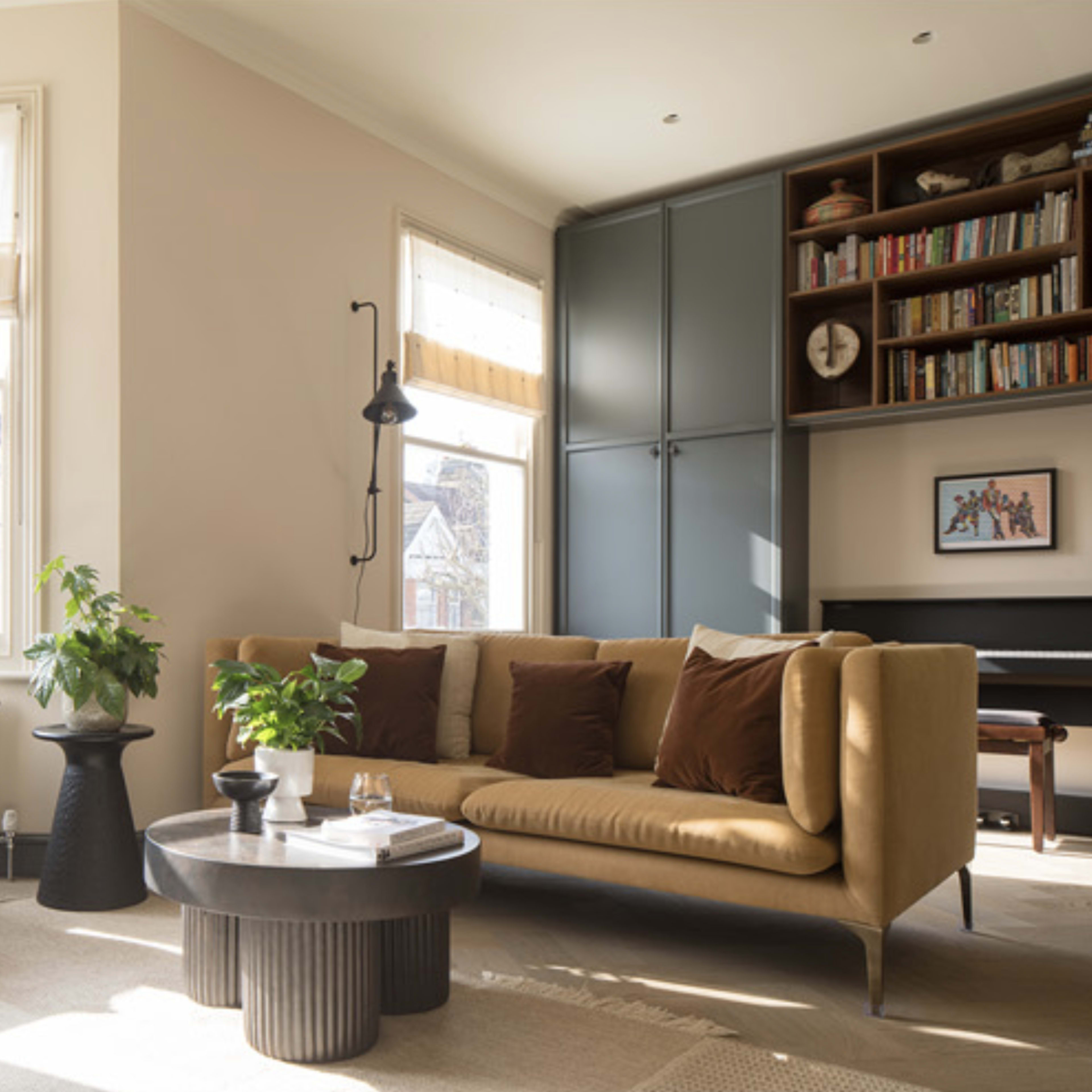 A cozy living room with a blue armchair, a tan sofa with decorative pillows, a circular coffee table, and bookshelves in the background.