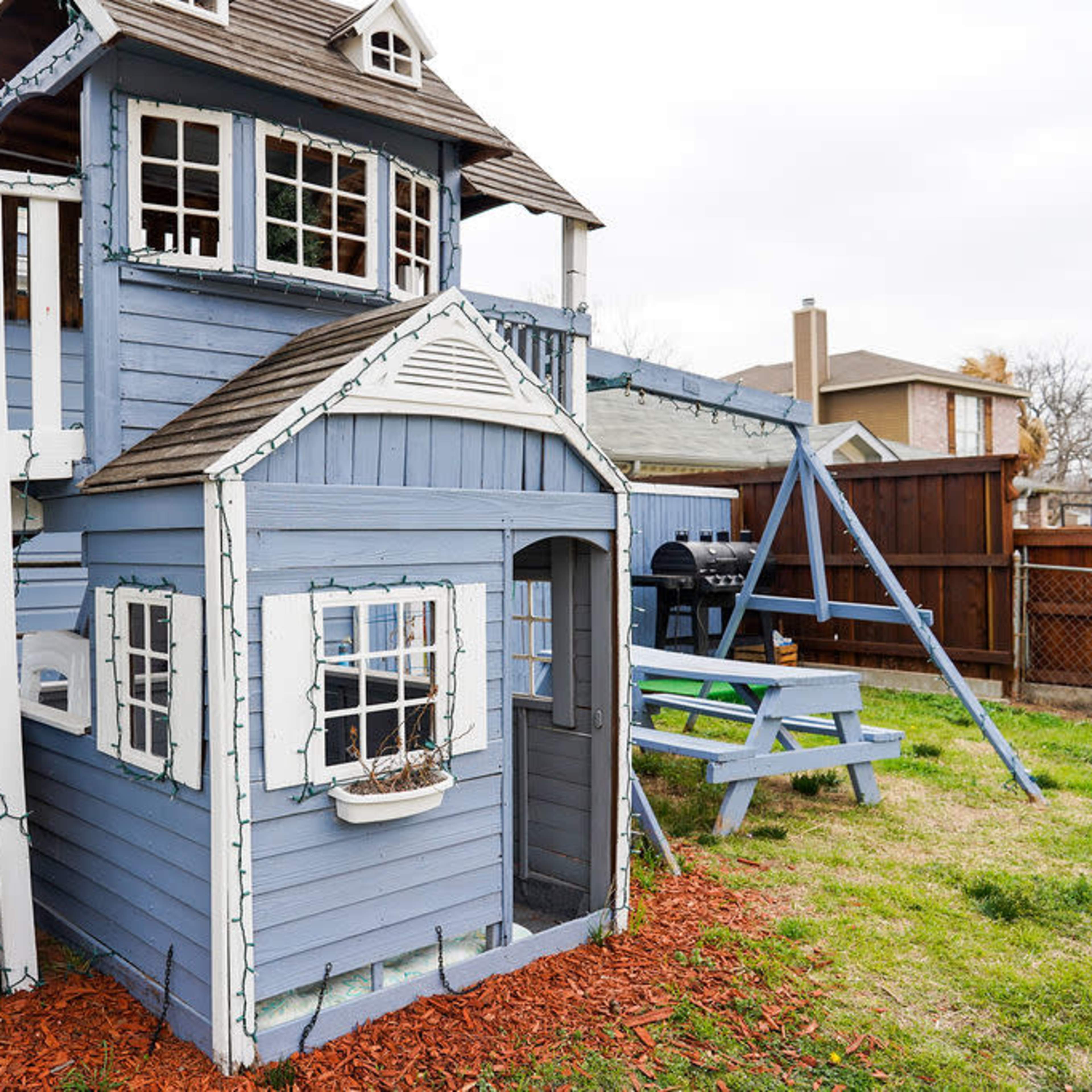 A blue playhouse with a slide, situated in a grassy yard with a picnic table nearby.