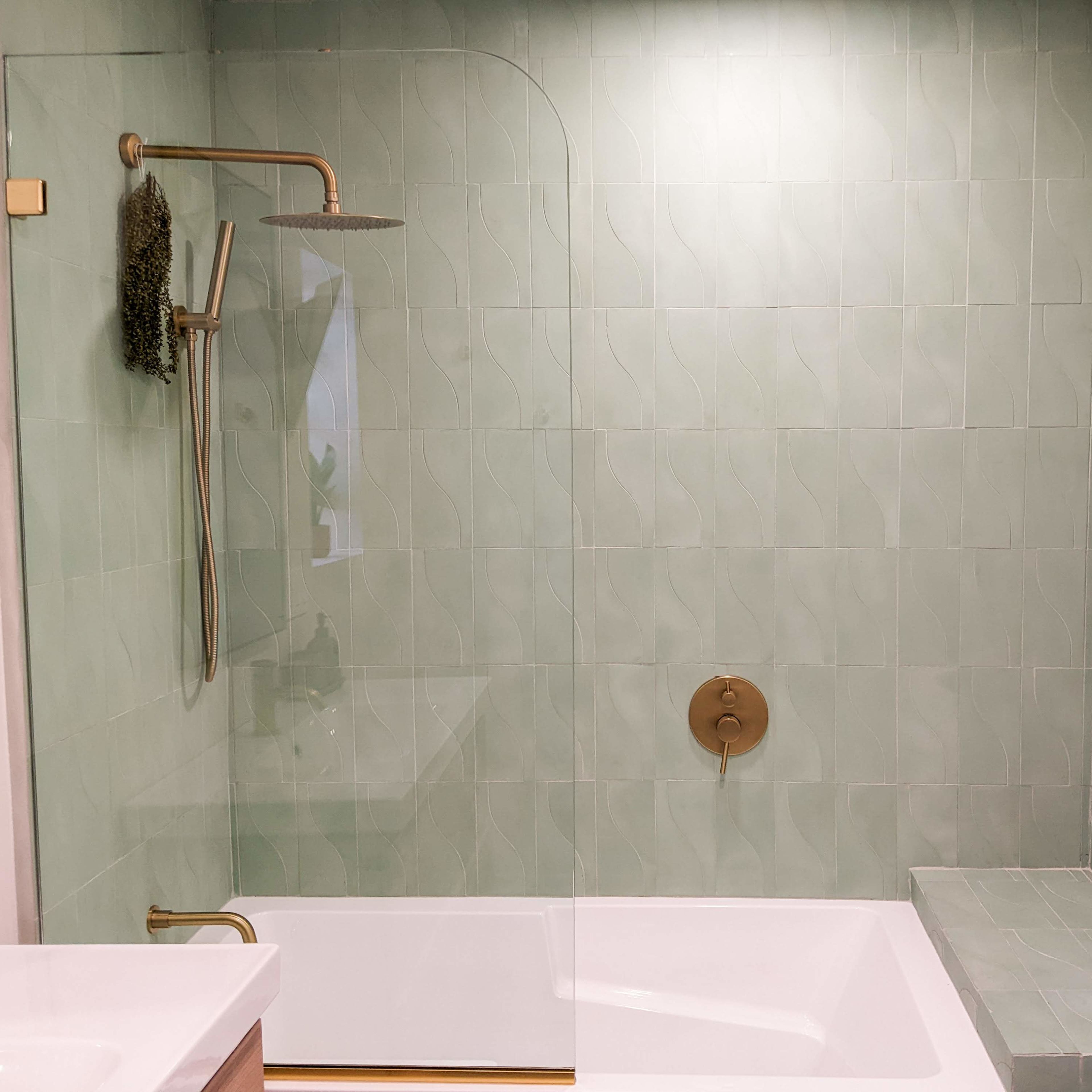 A modern bathroom featuring a glass shower enclosure with green tiled walls and a bathtub.