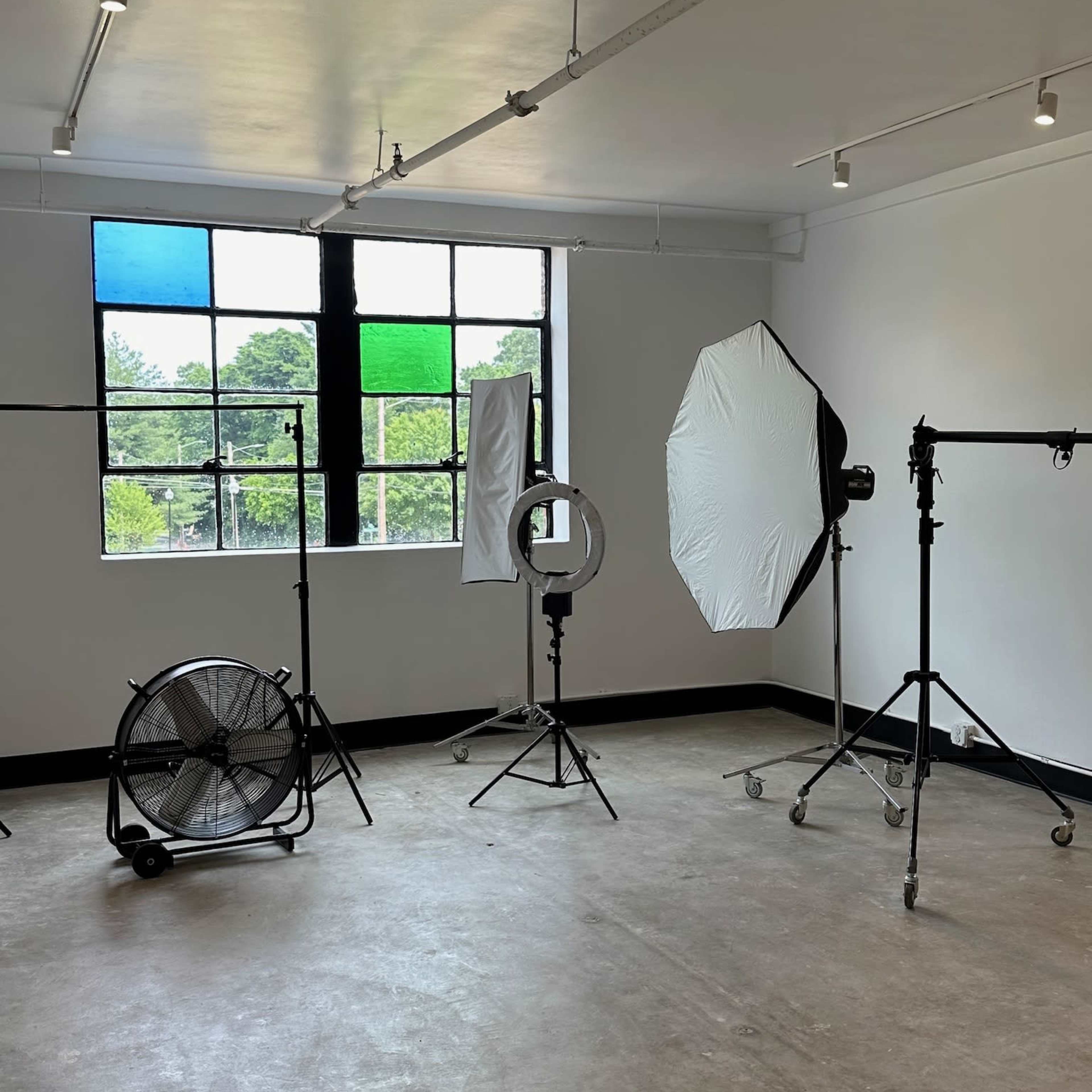 A photography studio with lighting equipment, backdrops, and a fan positioned near large windows.