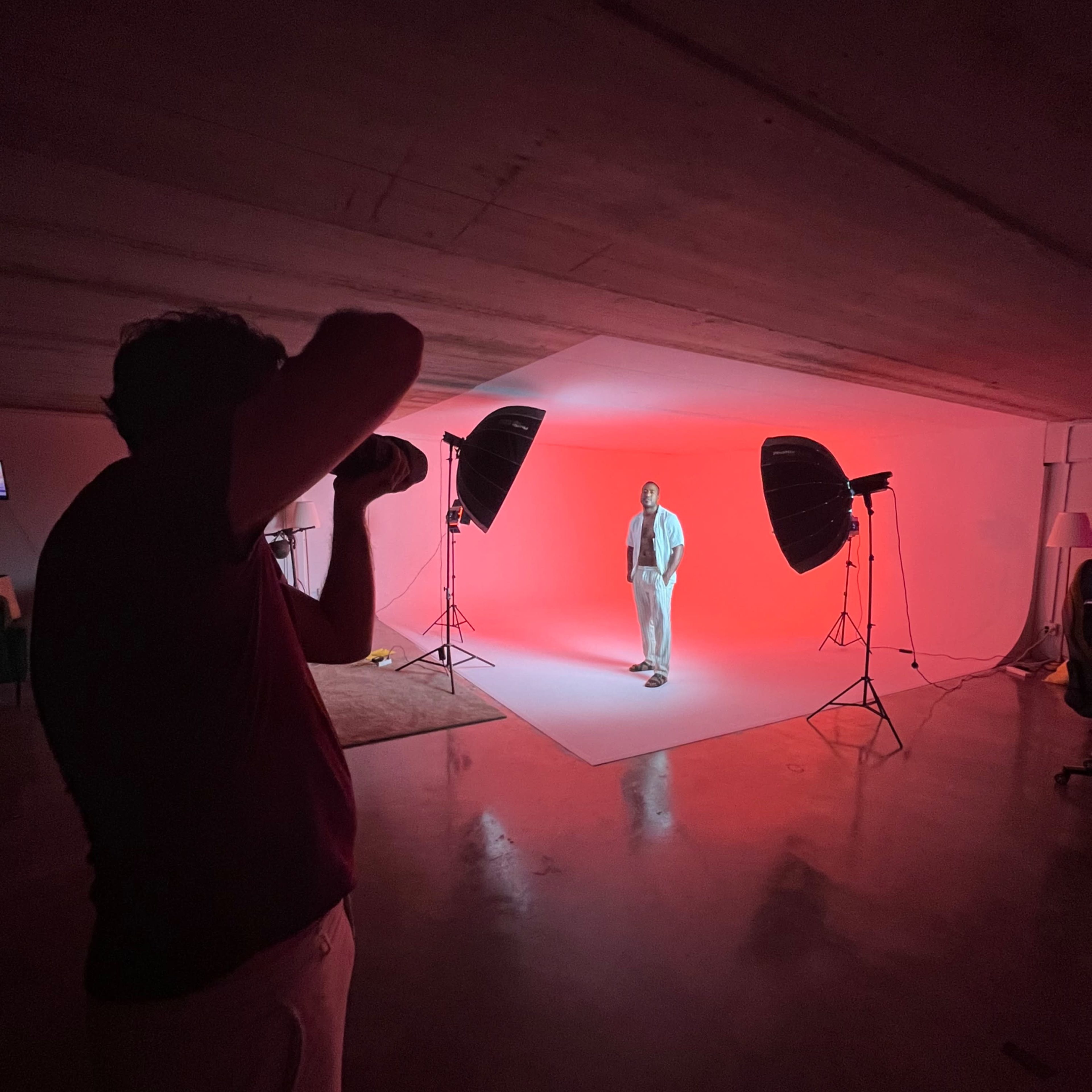 A photographer captures an individual posing under bright studio lights against a red backdrop.