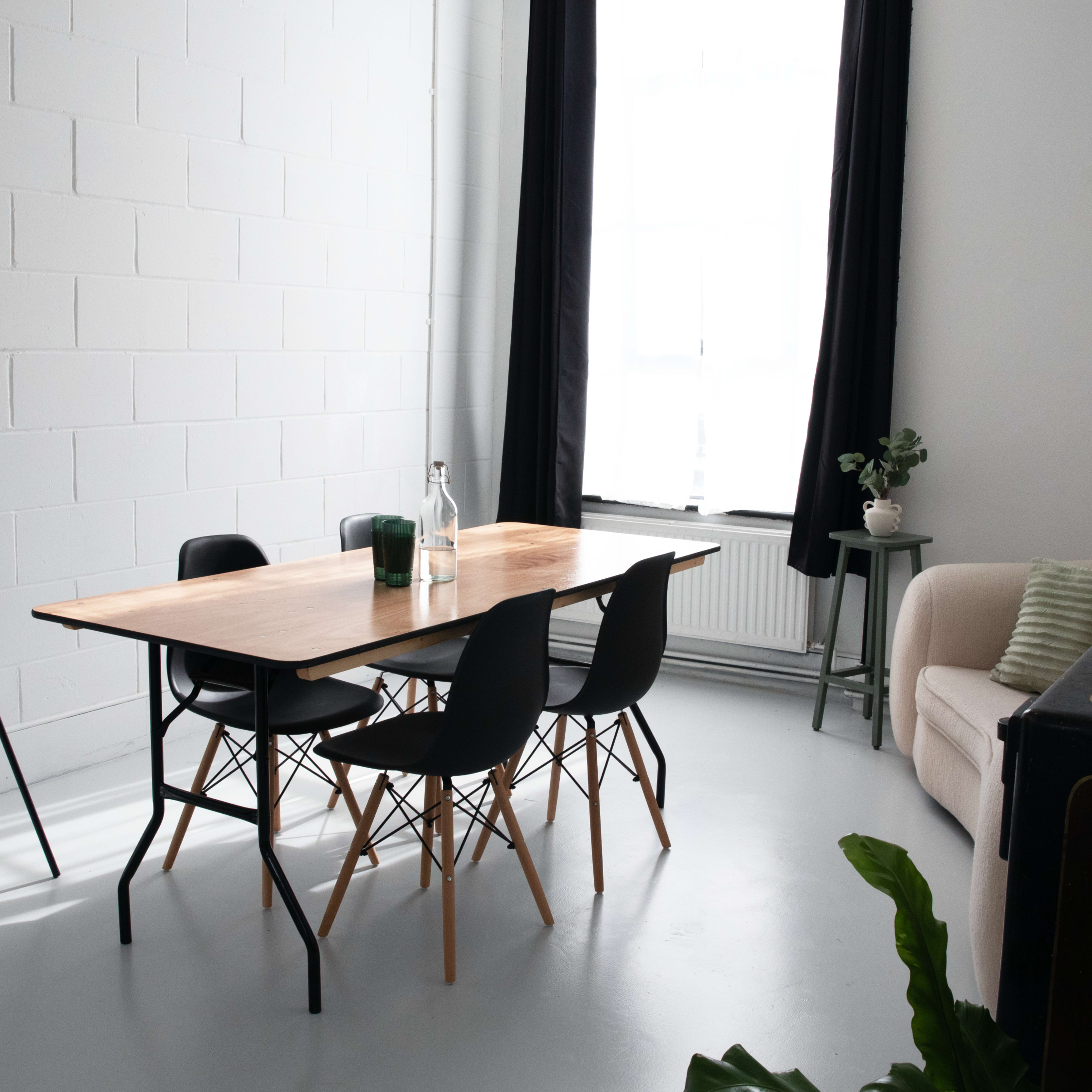 A bright, minimalist meeting room features a wooden table surrounded by black chairs, a whiteboard on an easel, and a sofa against the wall.
