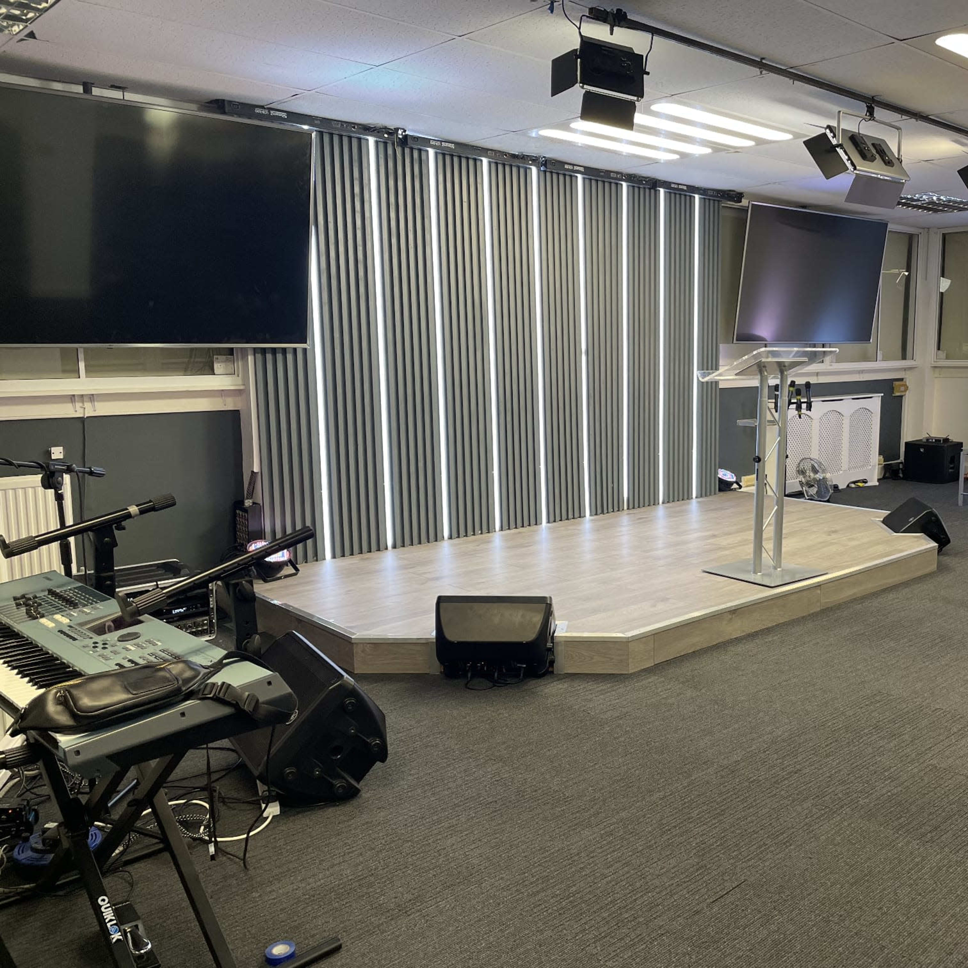 A stage setup in a room with two large screens, a podium, musical instruments, and seating arrangements.